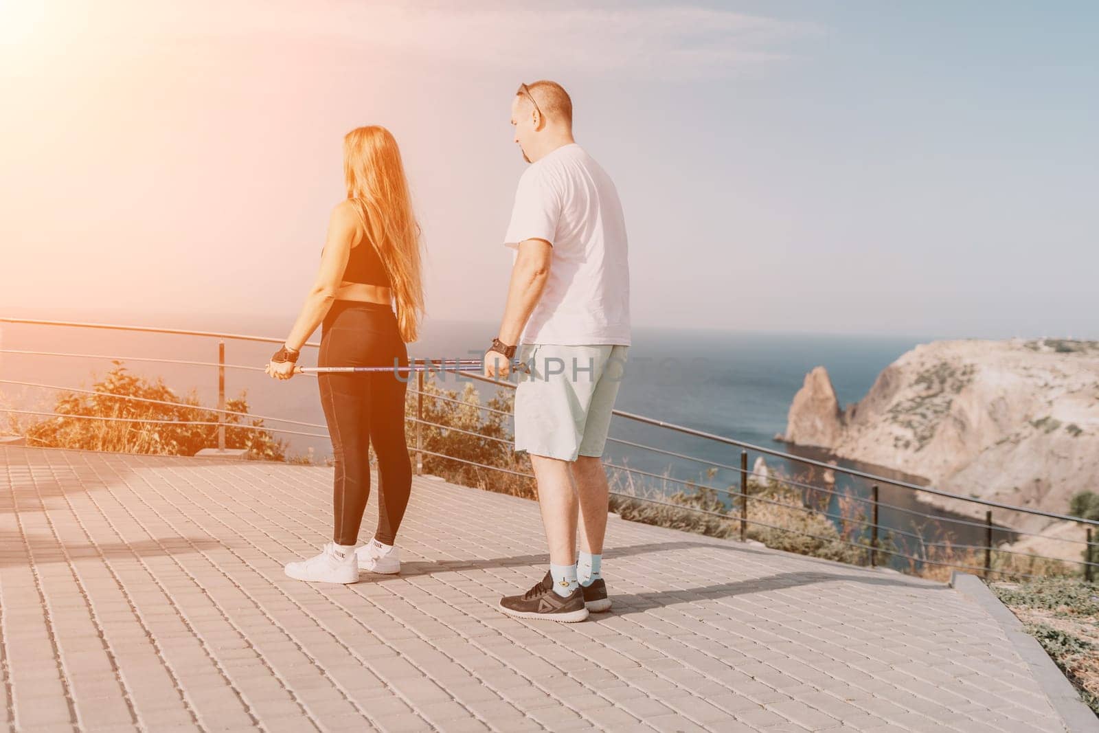 Happy Middle aged couple or friends practicing nordic walking in park near sea. Mature couple with trekking poles walking, practicing Nordic walking outdoors. Aging youthfully and sport concept.