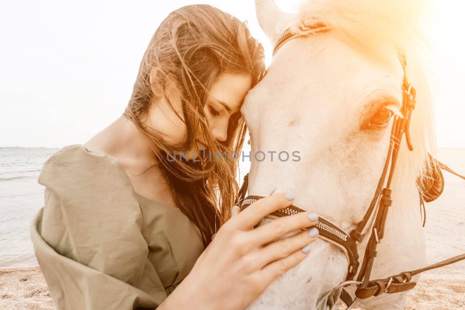 A woman in a dress stands next to a white horse on a beach, with the blue sky and sea in the background