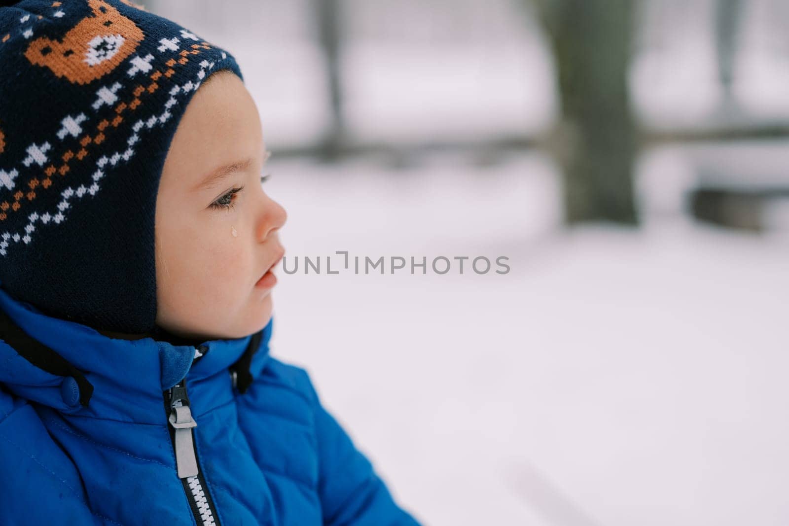 Little girl with a tear rolling down her cheek stands in the snow and looks into the distance. High quality photo