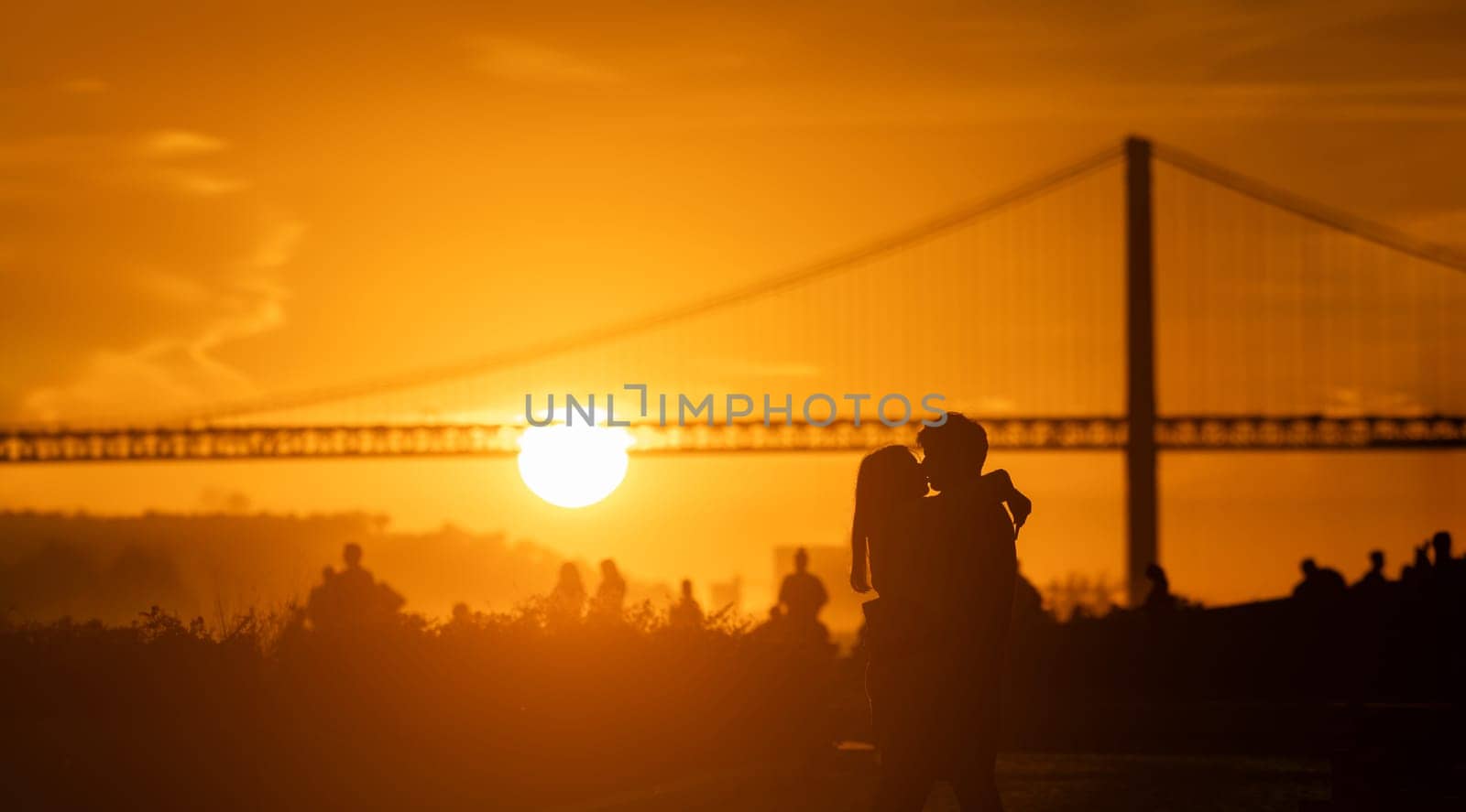 A couple of people that are kissing in front of a bridge