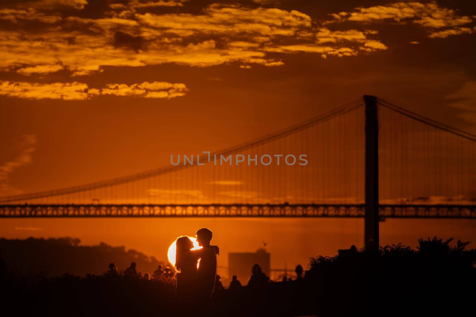 A couple kissing in front of a bridge at sunset