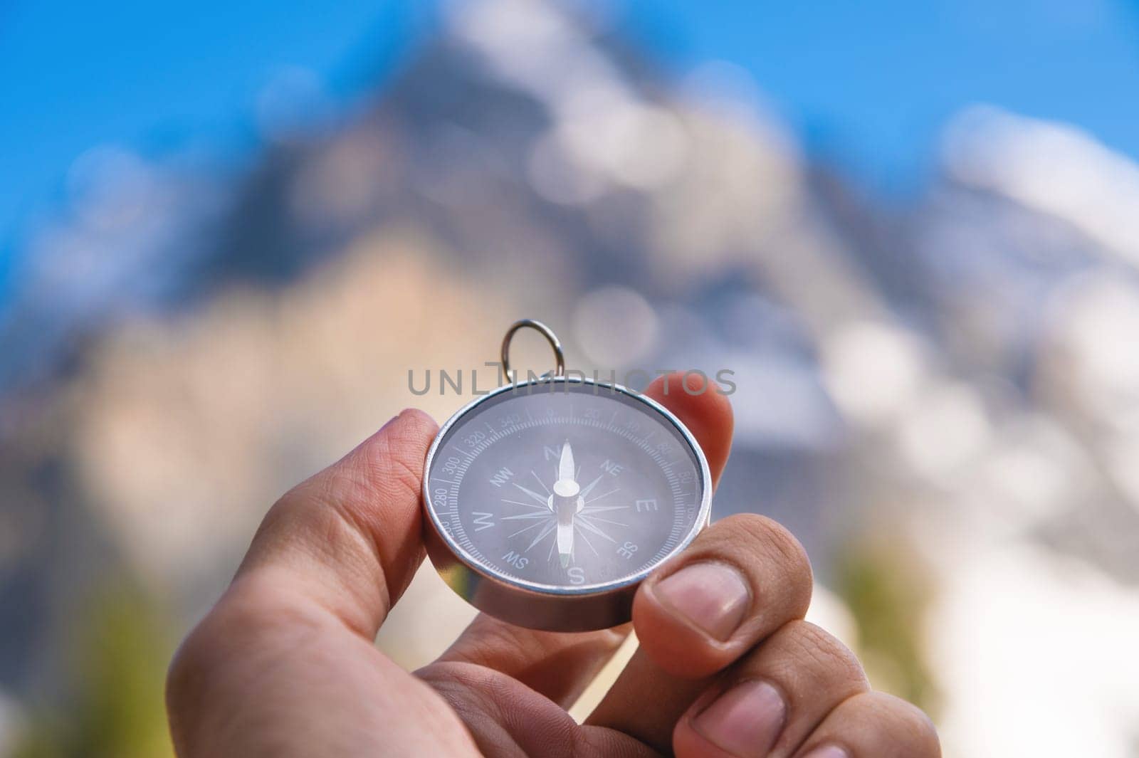 Compass in hand. Navigation and travel direction concept. A man with a compass in his hand against the background of high powerful mountains on a sunny day.