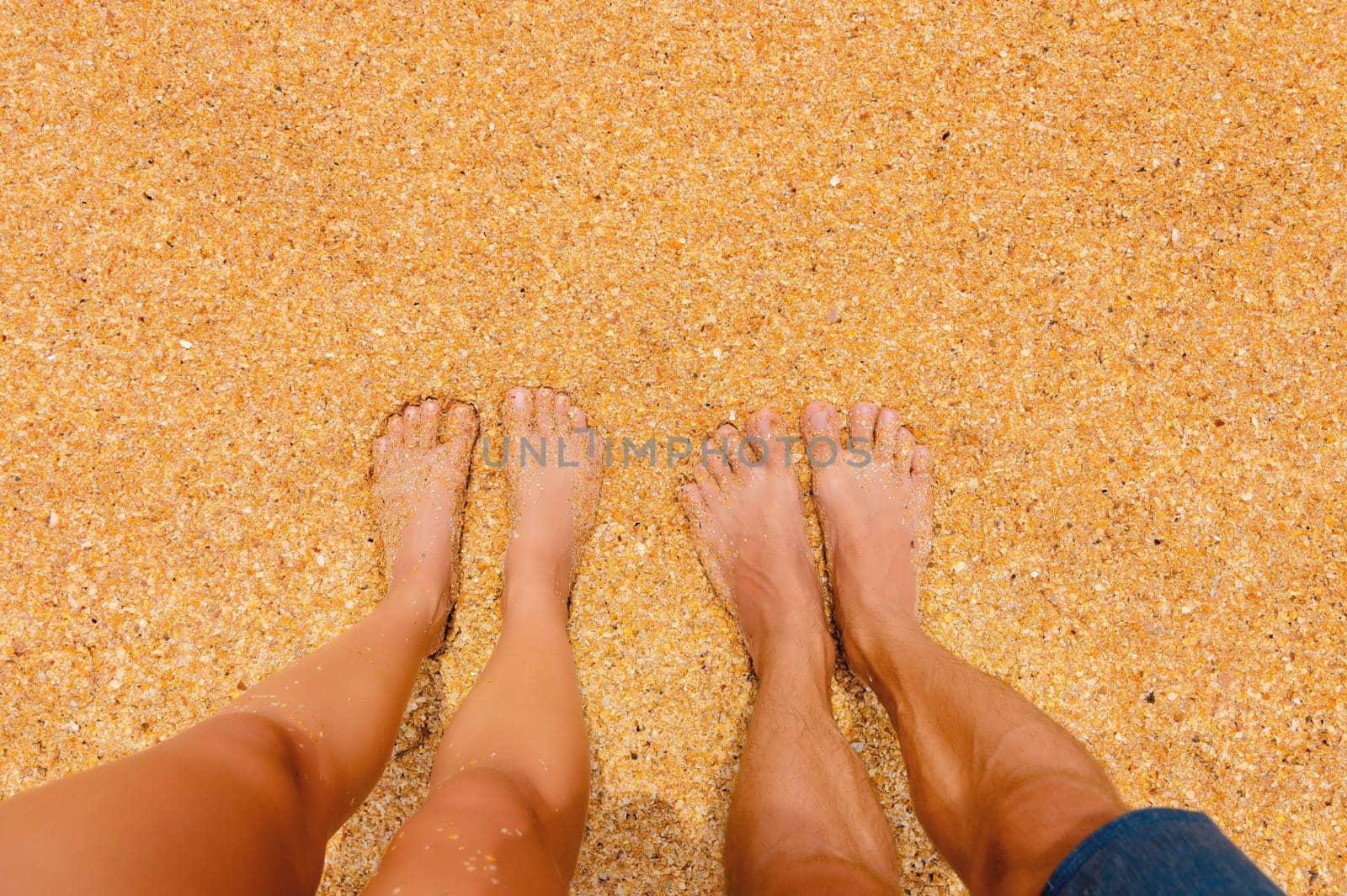 A man and a woman stand barefoot on the sand on the beach. Pair of feet in nature, summer vacation trip, outdoor date. Close-up, first person view