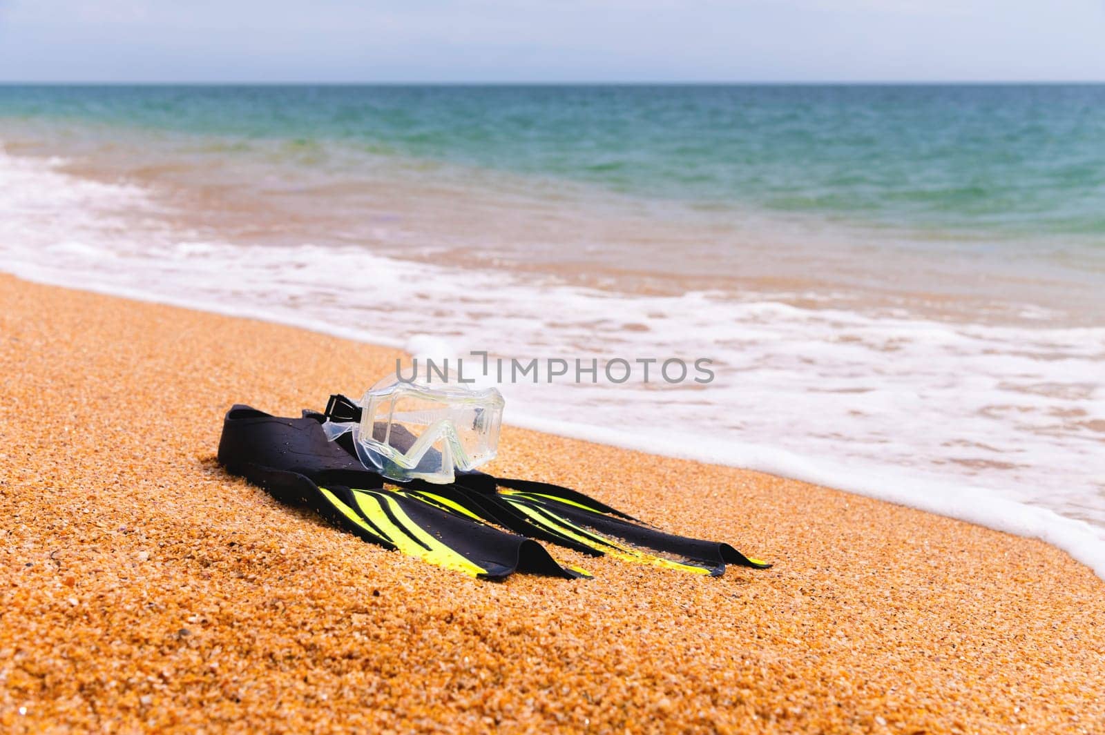 diving goggles, snorkel and fins on the beach with yellow sand. close-up of snorkeling equipment, against the backdrop of sea waves.