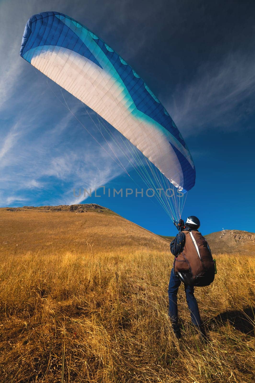 paraglider is preparing to take off from a mountain on a sunny day. paraglider taking off from yellow grass, against the background of blue sky and mountains by yanik88