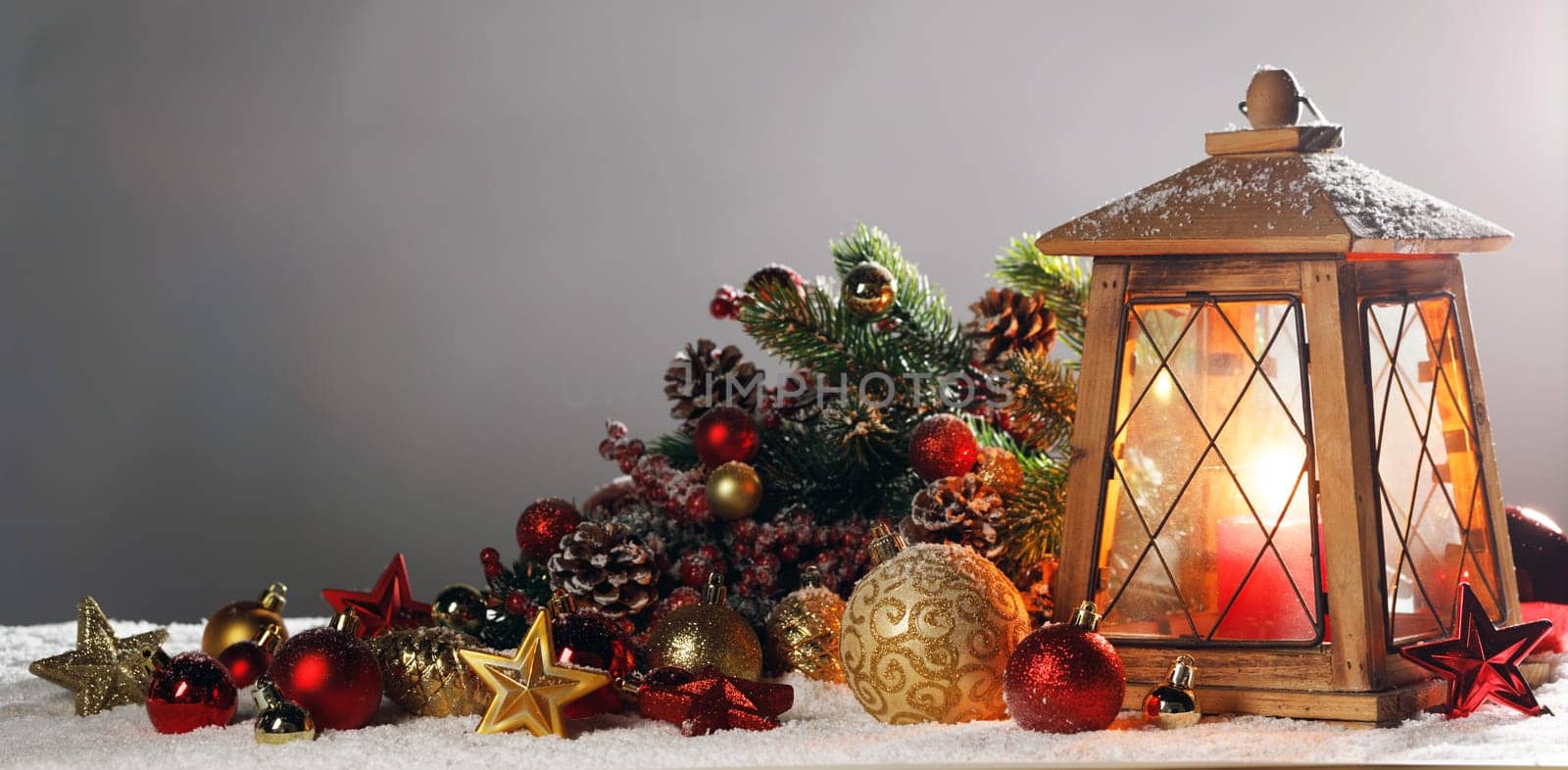 Christmas composition of lantern colorful ornaments balls stars candles and fir tree branches on snow