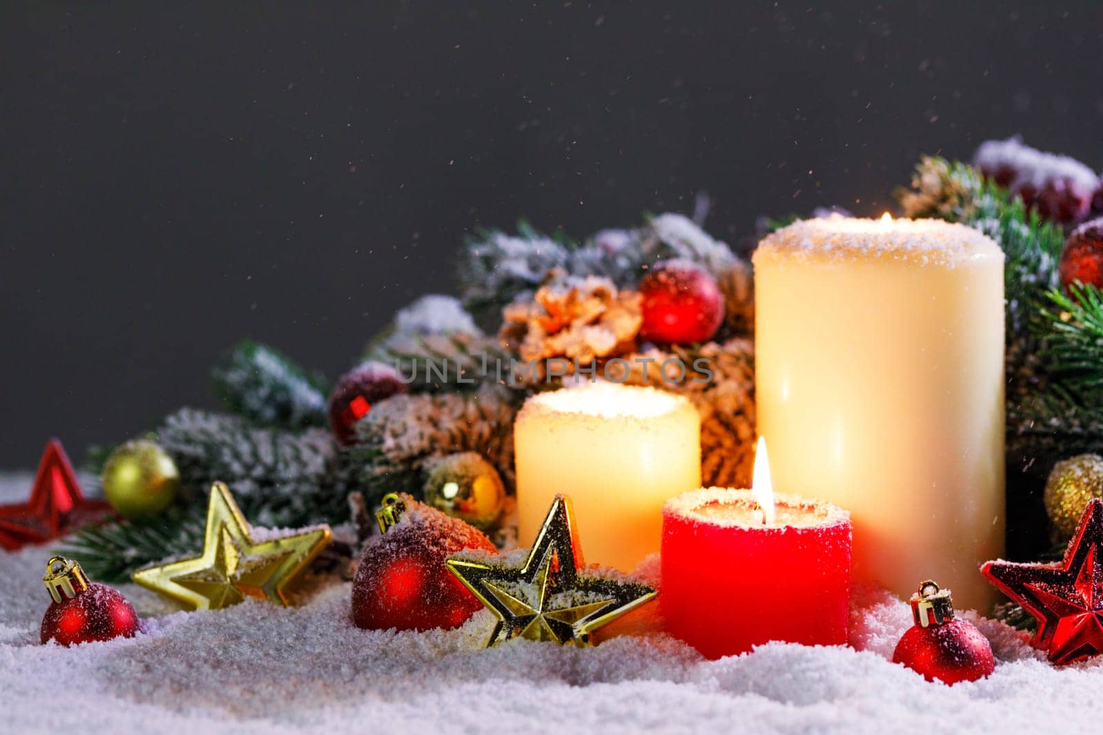 Christmas candles with traditional decorative stars , red baubles , pine cones and green branches on snow