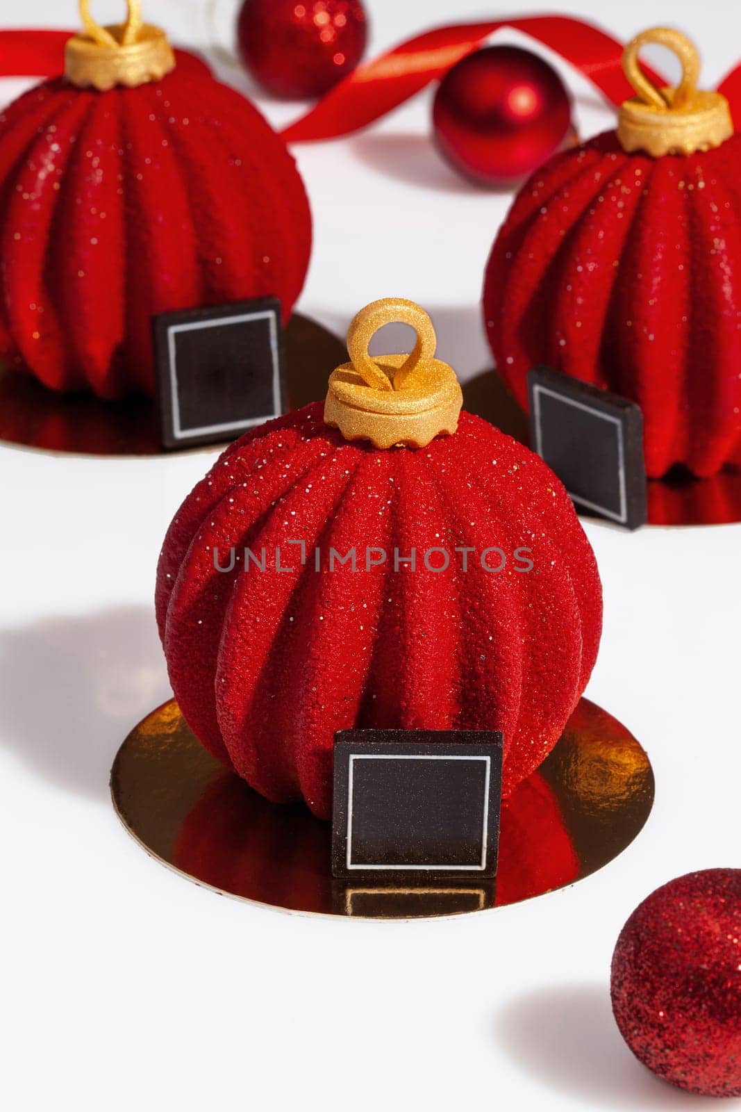 Delicious treats for New Year celebration. Handmade authors desserts in shape of red glazed Christmas balls on golden serving cardboard. Festive mood concept