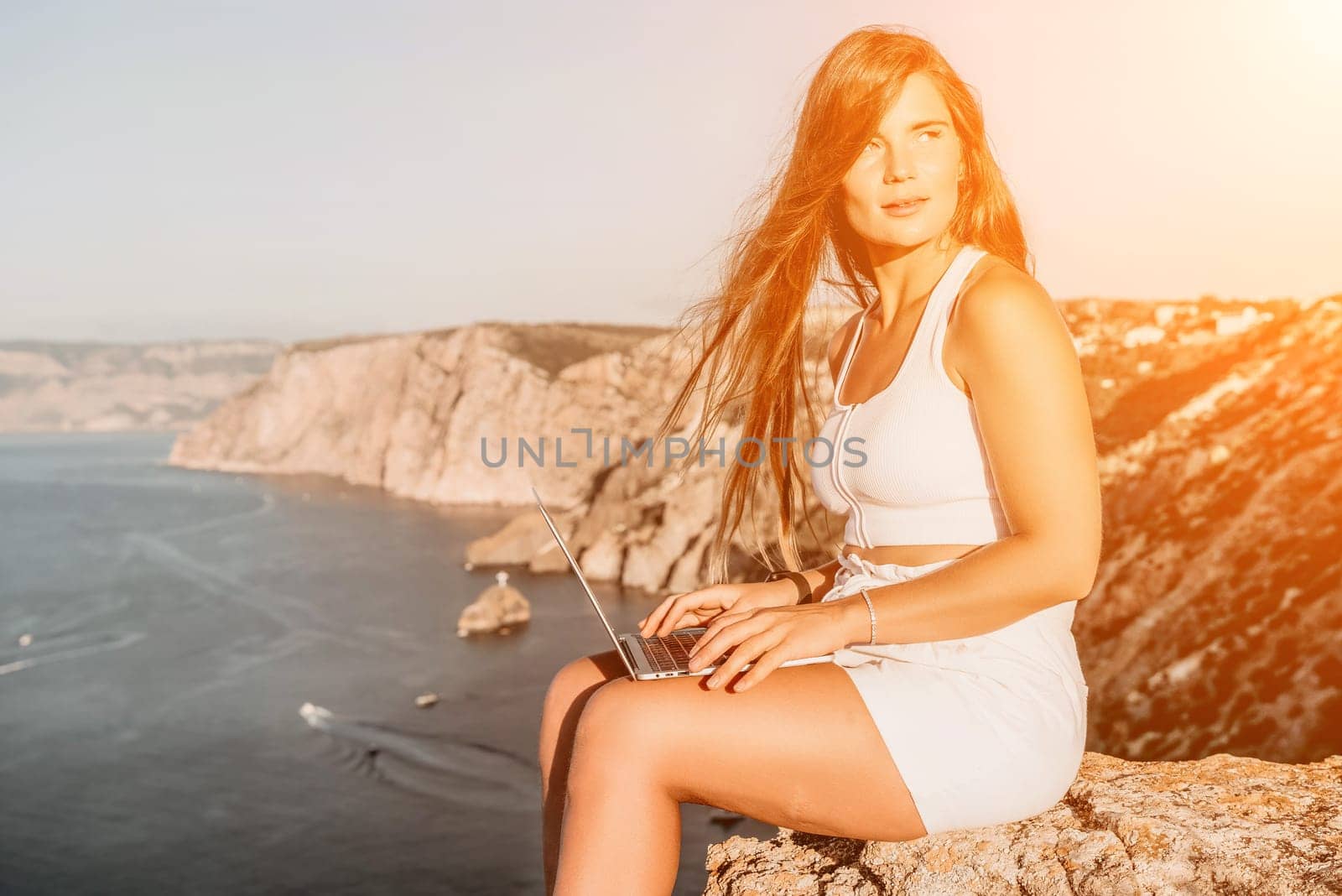 Digital nomad, Business woman working on laptop by the sea. Pretty lady typing on computer by the sea at sunset, makes a business transaction online from a distance. Freelance, remote work on vacation by panophotograph