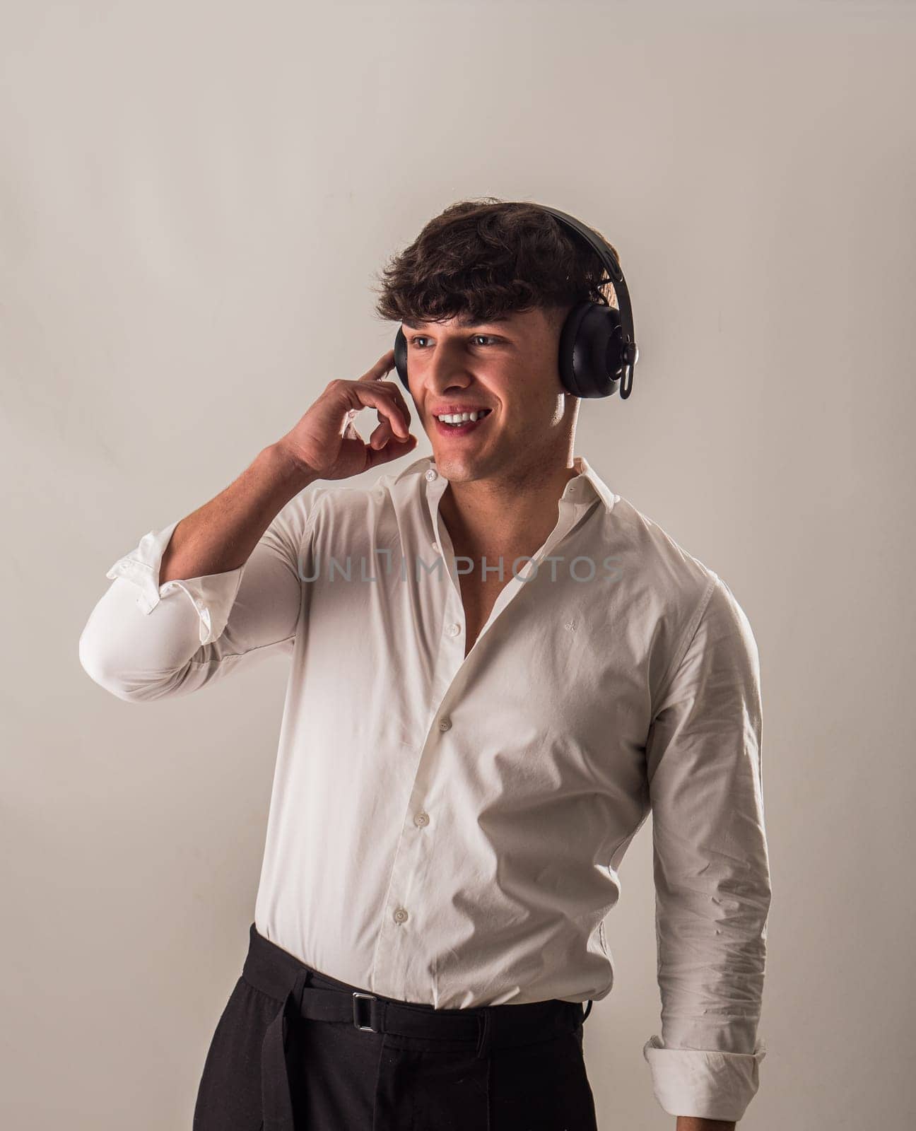 A young handsome man in a white shirt is listening to music on headphones, in studio shot