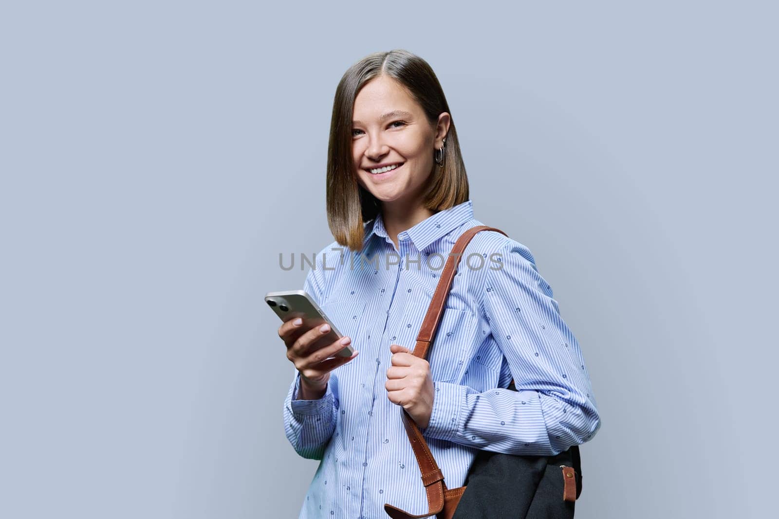 Young woman student with smartphone backpack on grey studio background by VH-studio