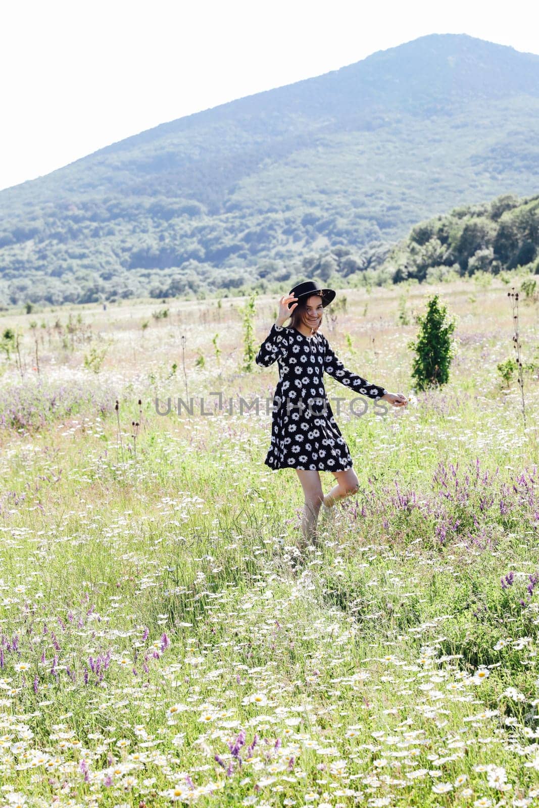 a woman in a hat walks in a field of flowers with daisies travel by Simakov