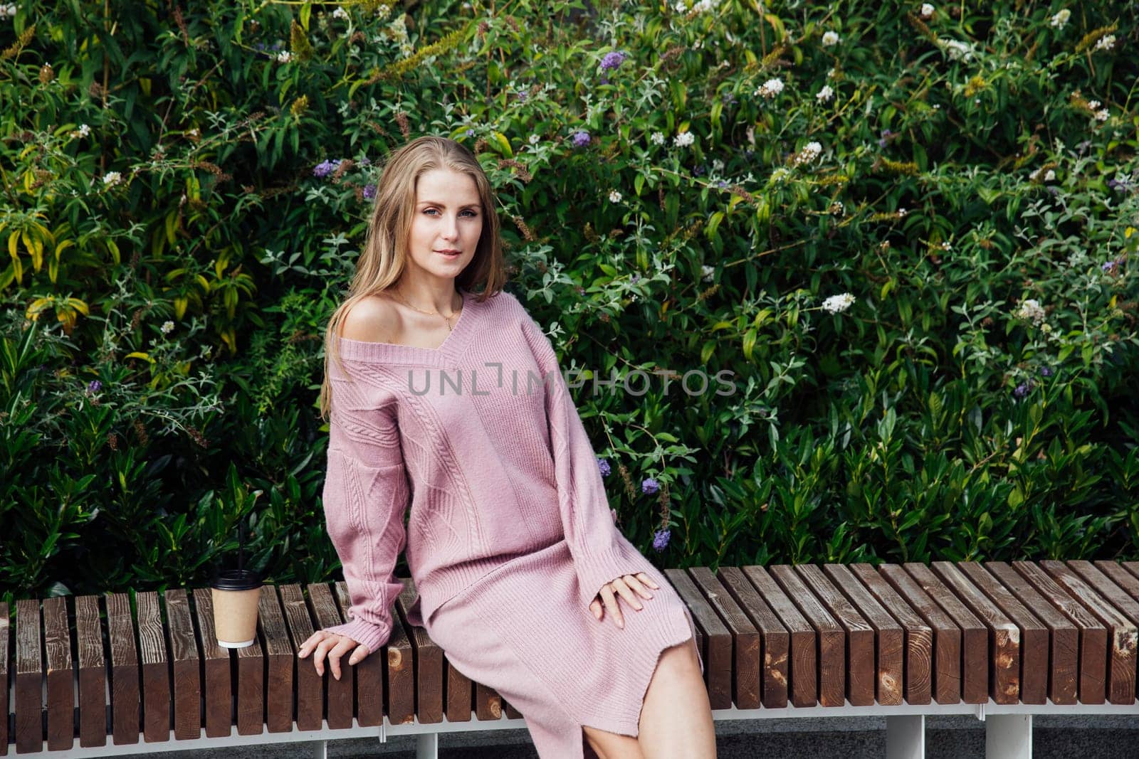 blonde woman sitting on bench by green bushes