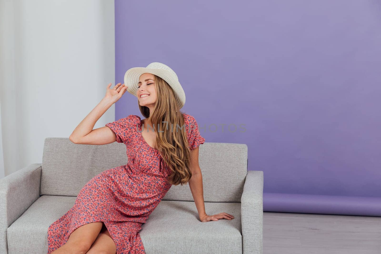 blonde in a beautiful dress and hat sits in a room on the couch rest by Simakov