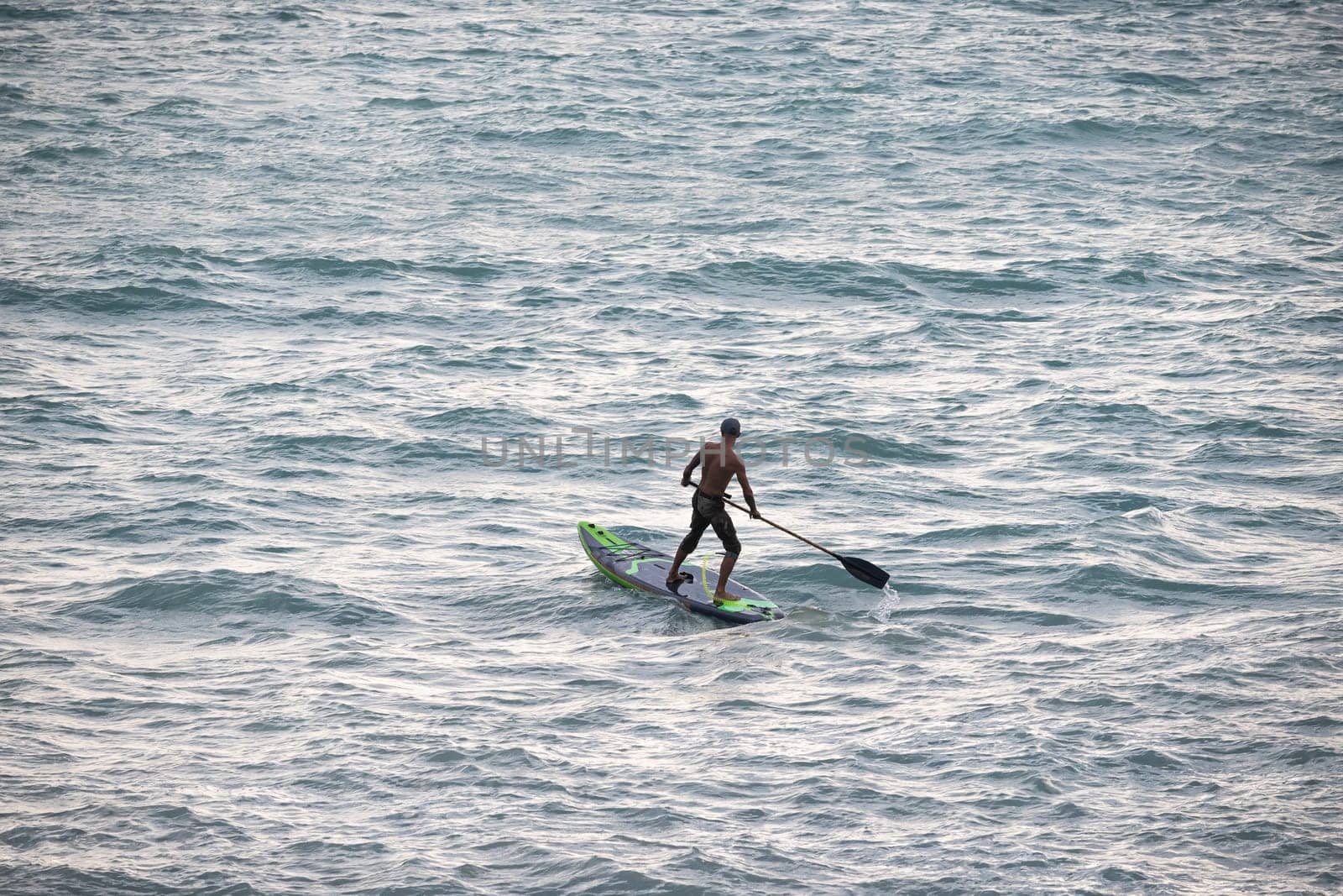 athletic wiry surfer guy swims with a paddle on sup board in the sea Stand up paddleboarding