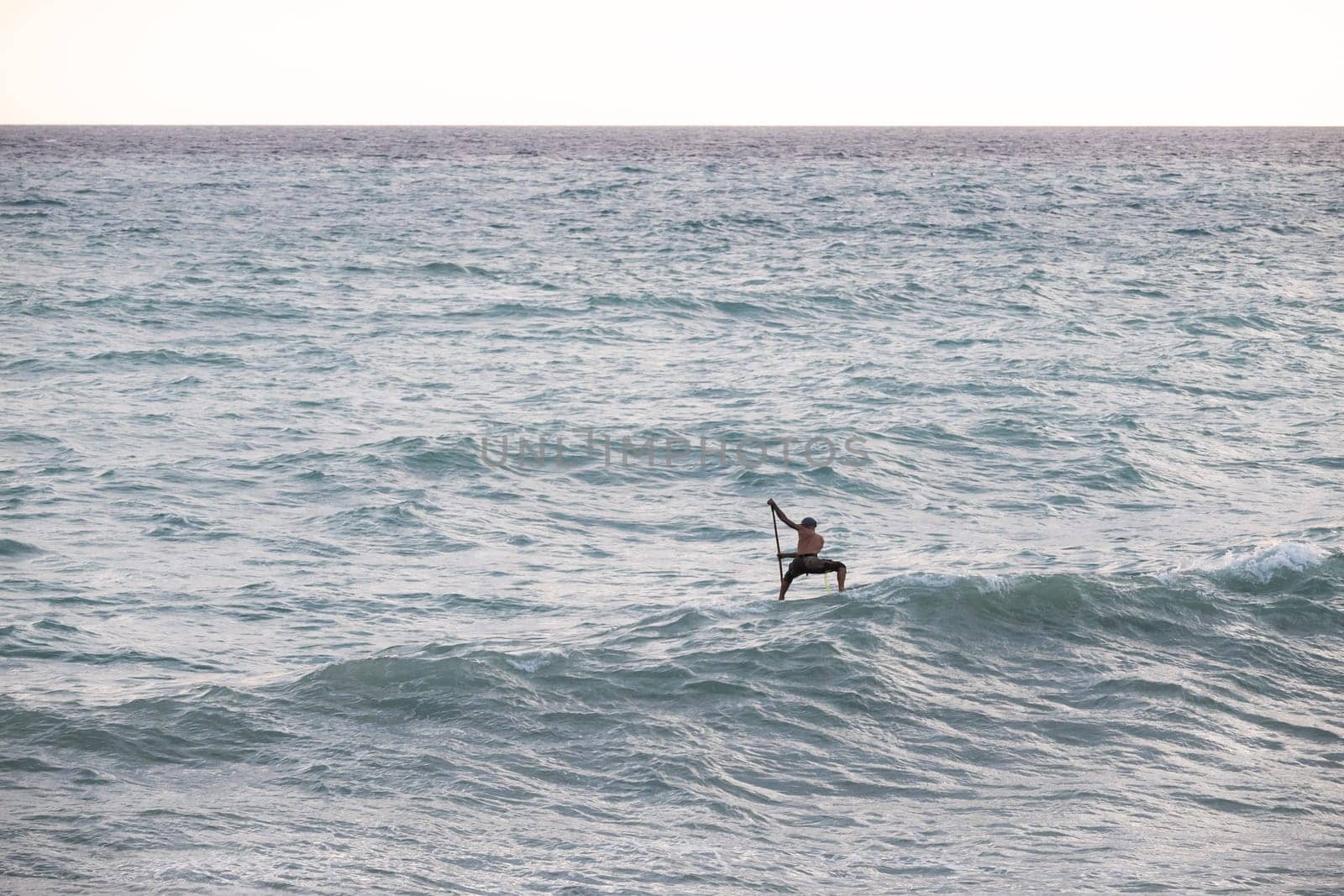 athletic wiry surfer guy swims with a paddle on a sup board in the sea Stand up paddleboarding by Rotozey