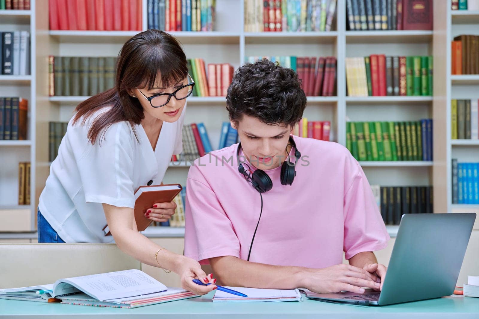 Woman mentor teaching male student in college library, exam preparation by VH-studio