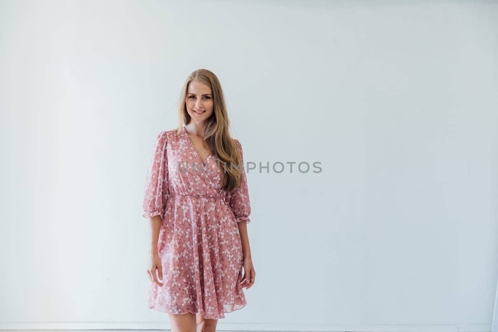 blonde woman in a pink floral dress poses in a bright room