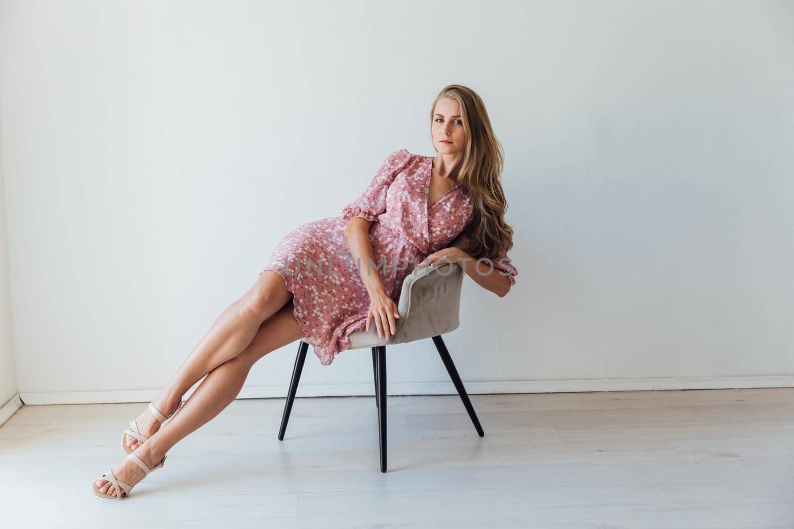 beautiful blonde woman in a colored pink dress sits on a chair by Simakov