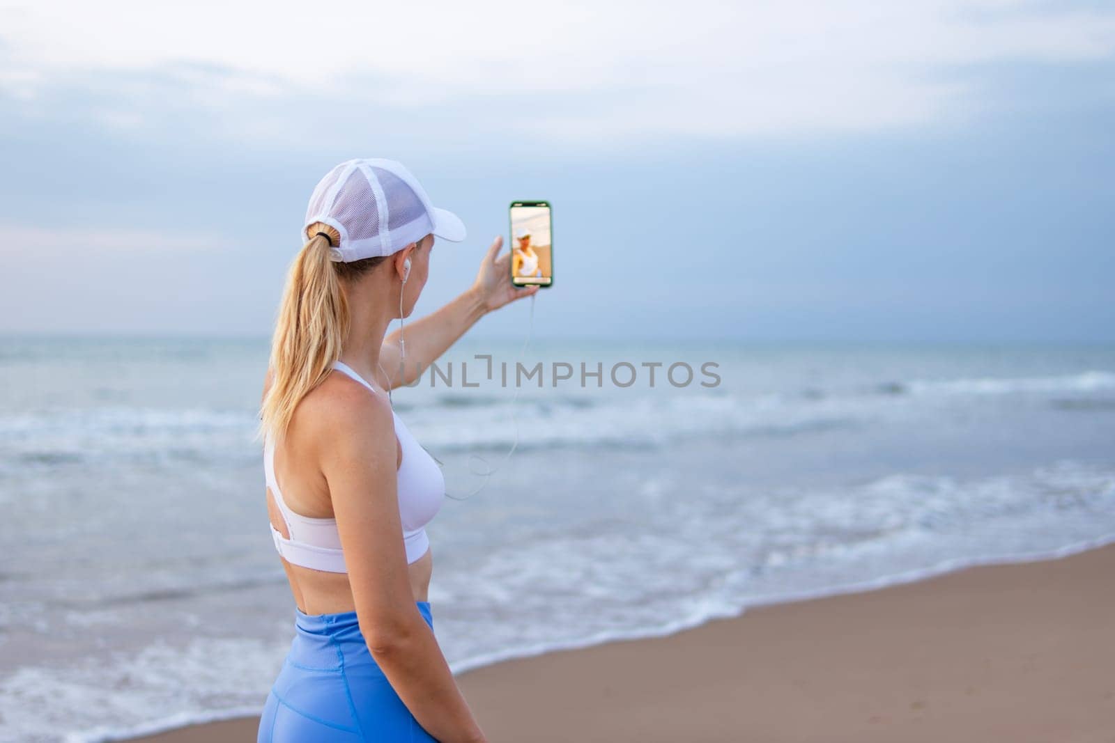 girl runner runs along the beach in sportswear. girl takes a selfie on the seashore before jogging. High quality photo