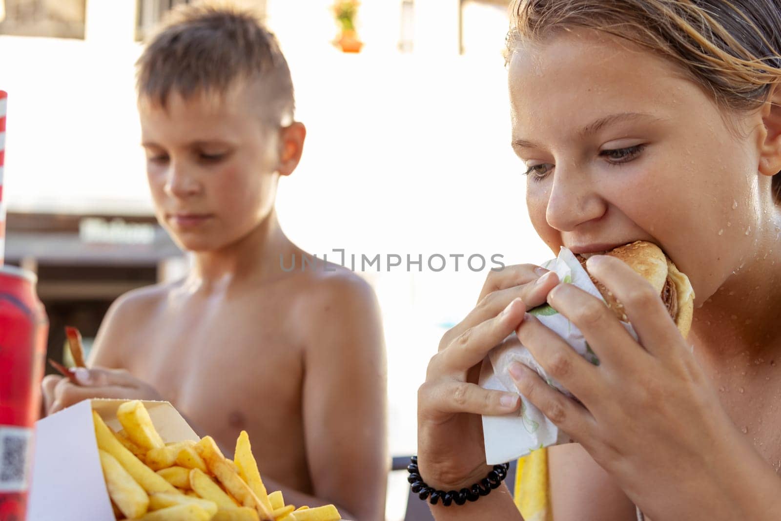 brother and sister of fair appearance eat burgers and fries on beach,summer vacation Focus on girl by PopOff