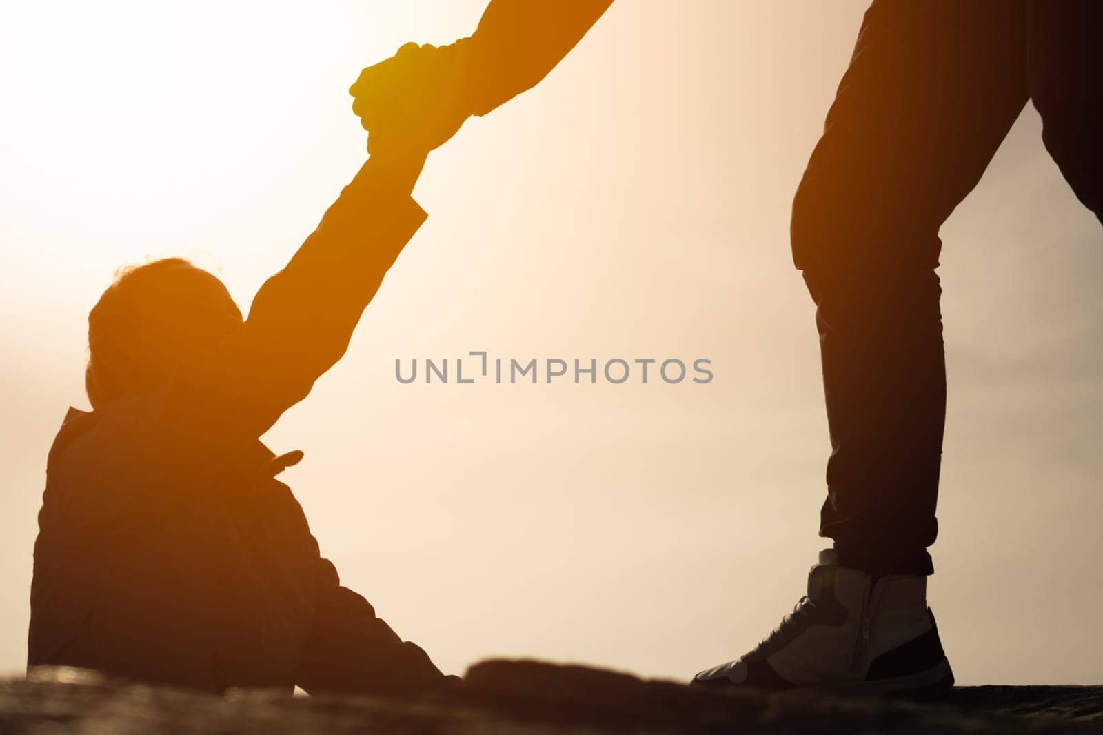 Giving a helping hand. Man helping female climber up a mountain.silhouette of a man gives a hand to a girl by PopOff