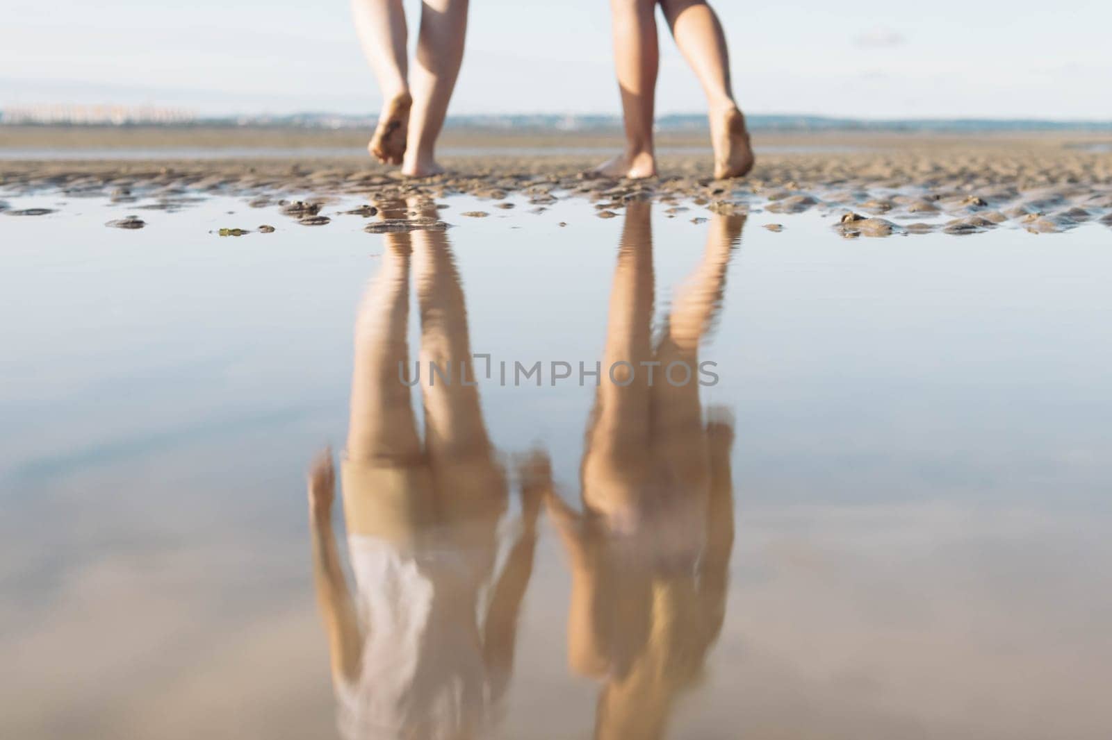 two girls walk on the sand reflection in the water in full growth photo of legs close-up .Beautiful landscape of the beach by PopOff