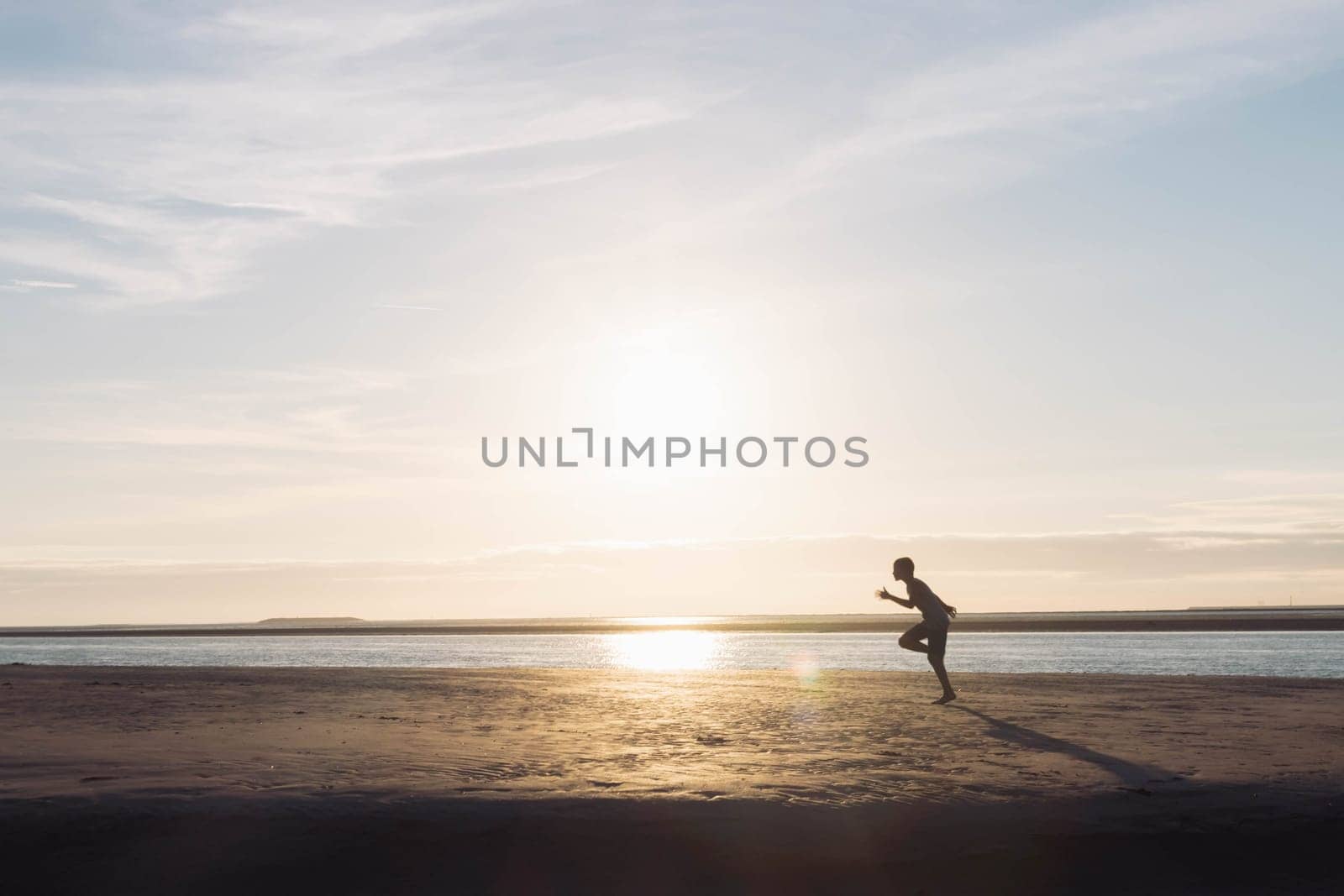 a boy runs on the beach at sunset, a silhouette of a child running on the beach on the sand near the water, there is a place for an inscription. High quality photo