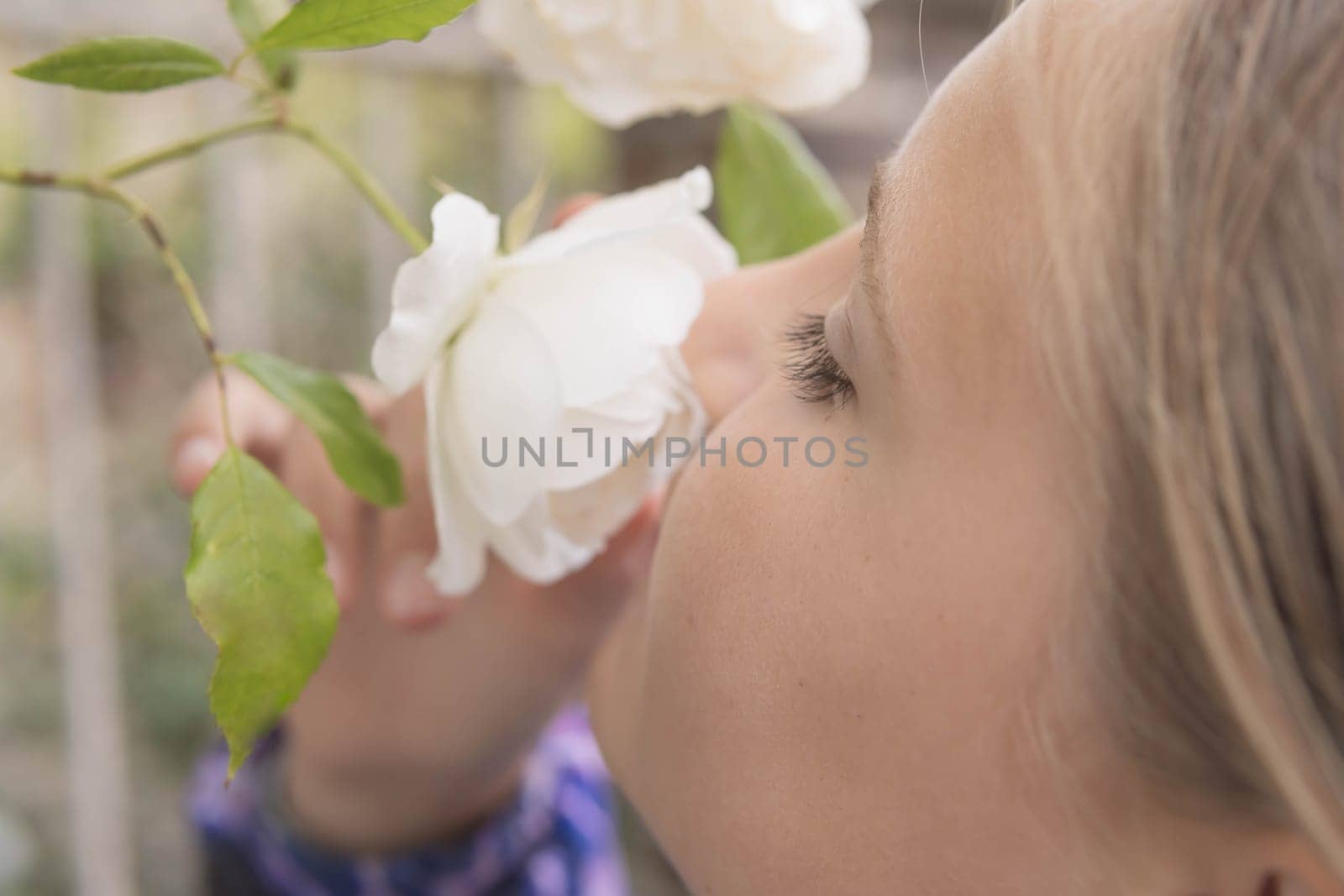 A teenager stands sniffing white flowers on a tree.Flowers in focus close-up by PopOff