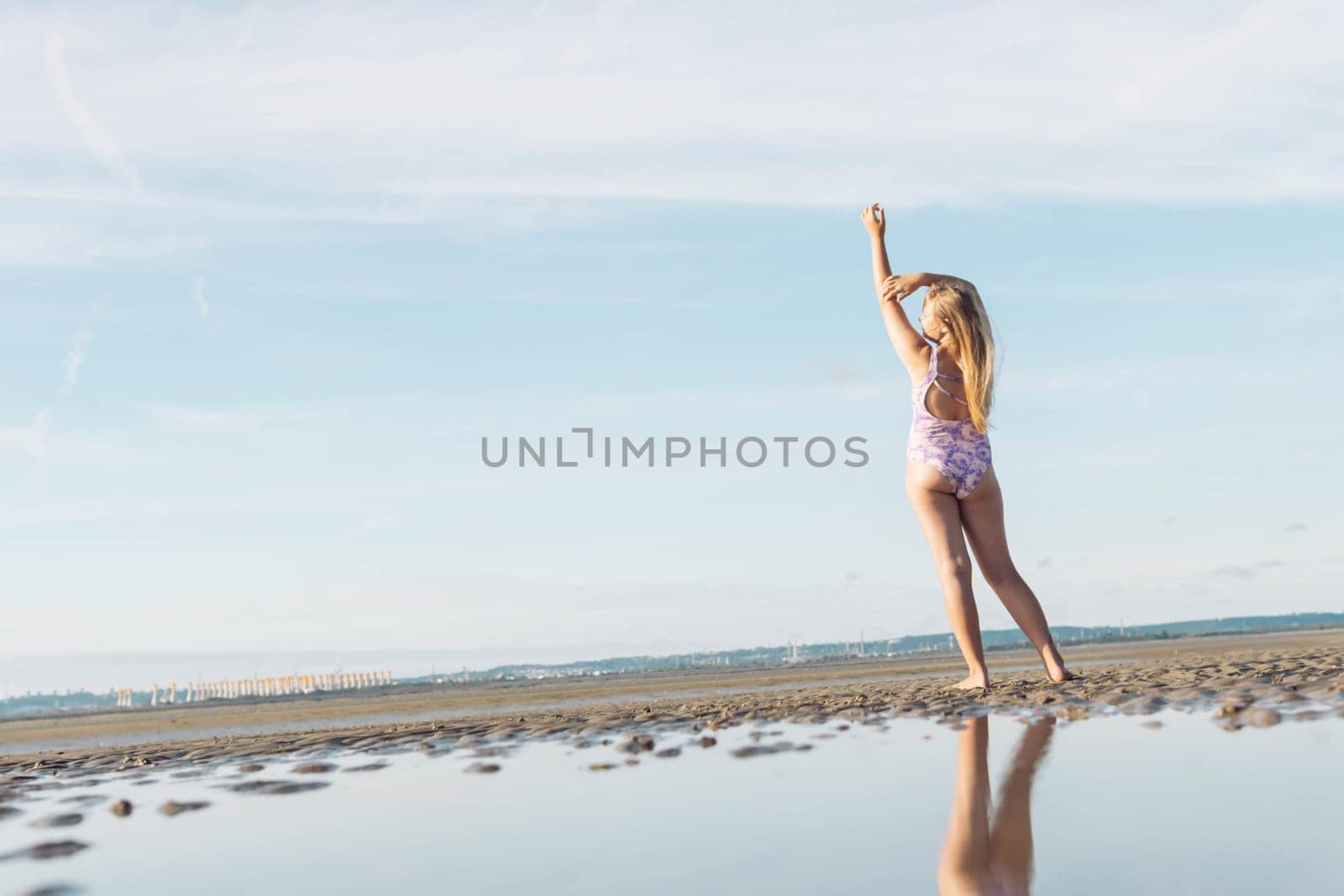 teenage girl in lilac swimsuit stands with her back to her full height on the ocean beach, in front of the photo there is water and on the left there is a place for an inscription. High quality photo