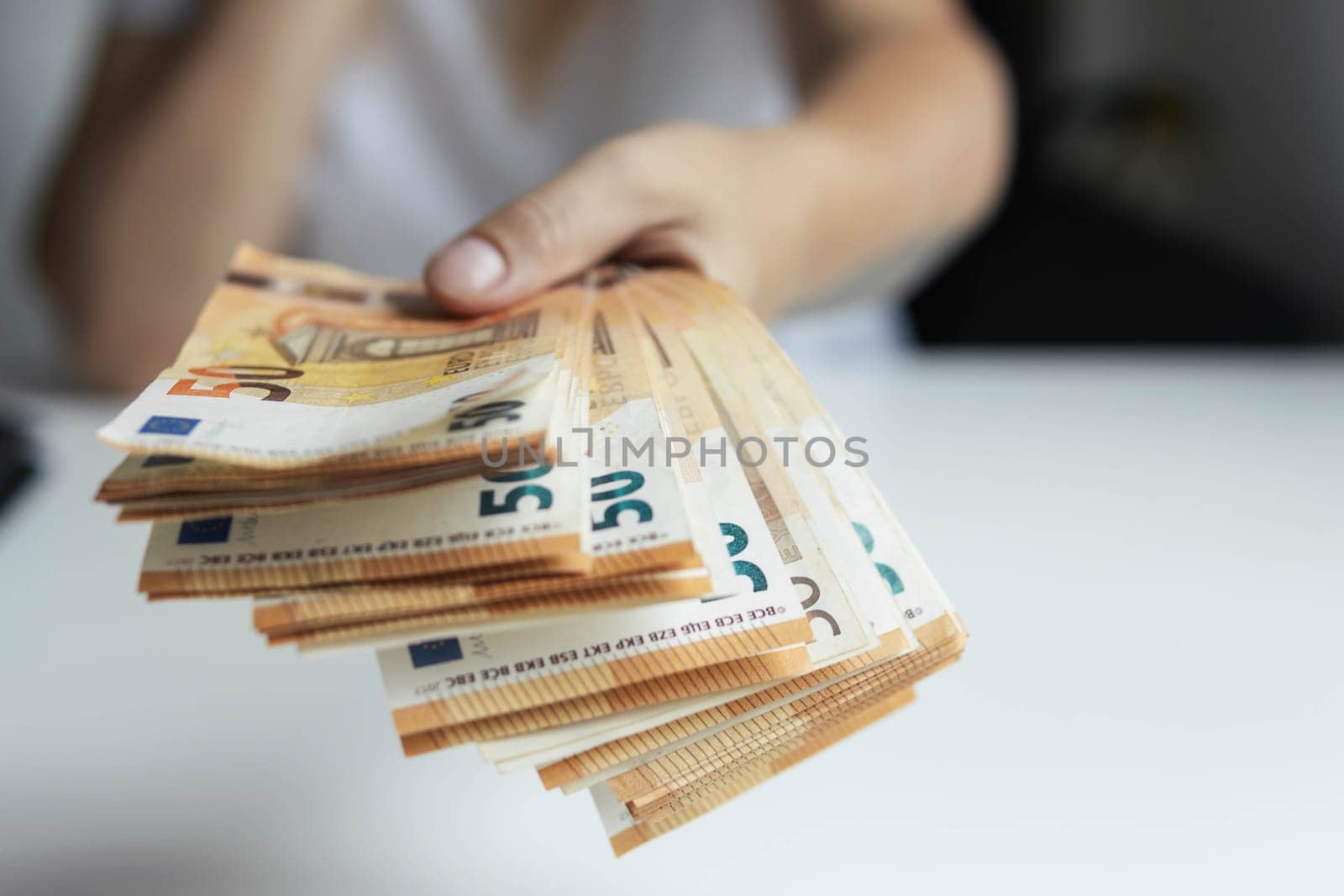 a girl in a white t-shirt stretches her hand forward holding euro 50 banknotes in her hand close-up focus on money background blurred. High quality photo