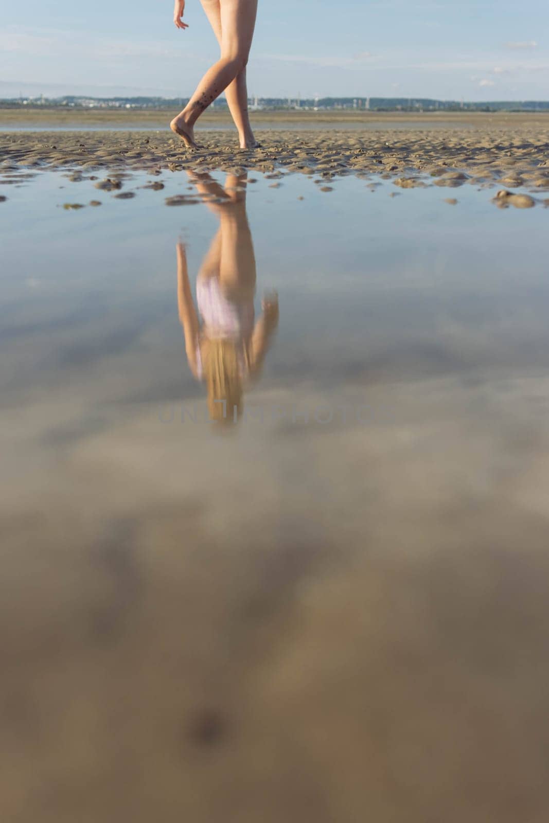 a girl in a bathing suit goes forward to the sea, a reflection in the water in full growth, a photo of women's legs on the beach by PopOff