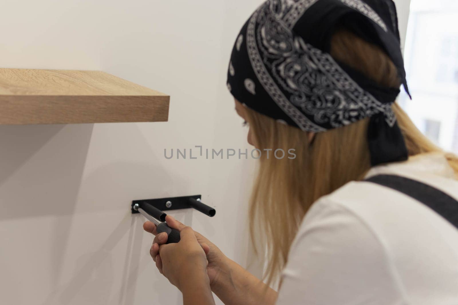 the girl spins the shelf for books on the wall. the girl is turned back to the camera close-up, blond hair and a black bandana on her head. High quality photo
