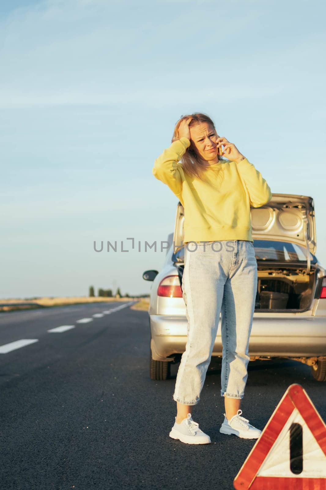 a girl of European appearance in a yellow sweater and jeans stands on the road near a broken car and speaks on the phone upset and holding her head, on the left there is a place for an inscription by PopOff