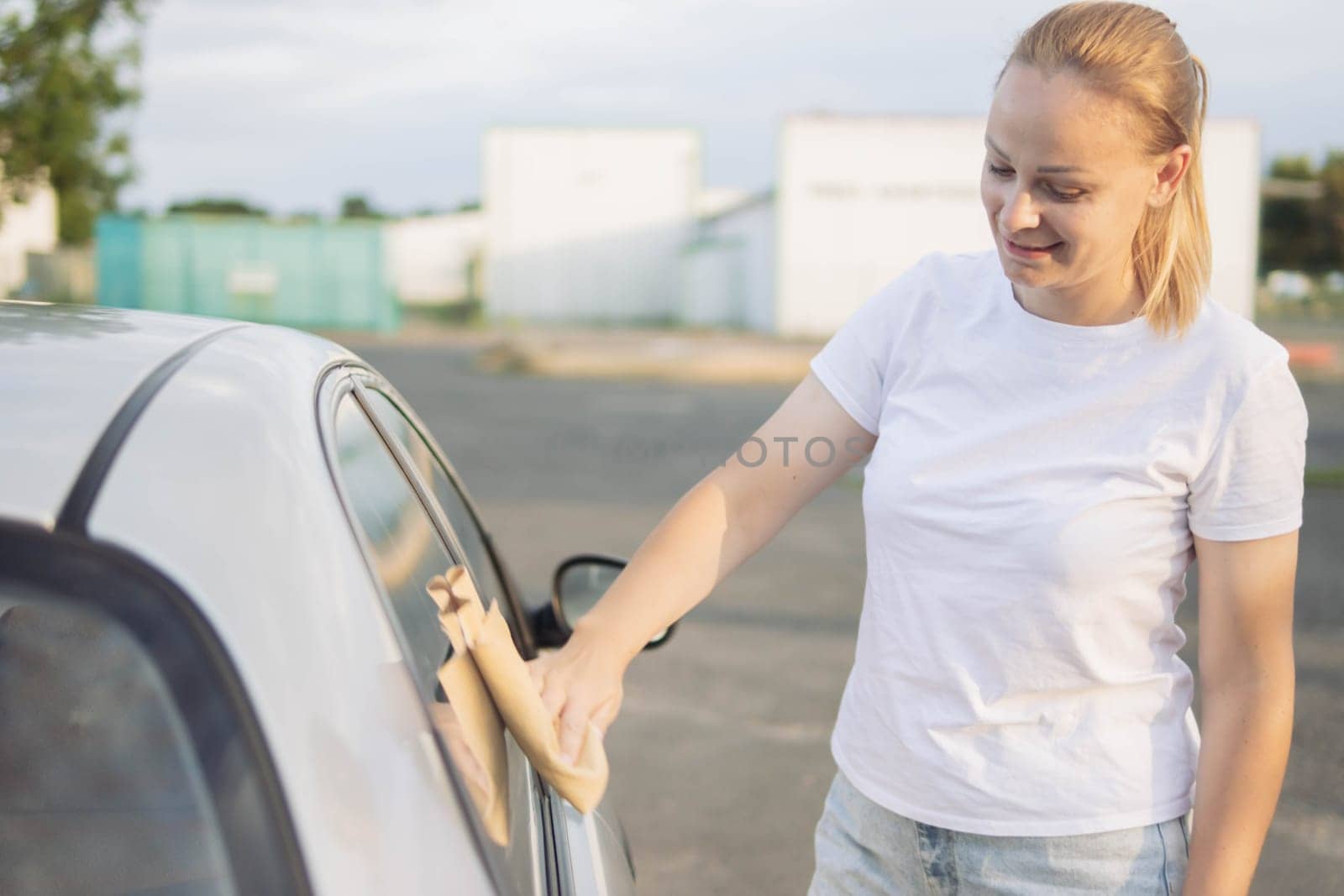 a girl of European appearance with blond hair in a white T-shirt and jeans,wipes the car after washing with a special yellow rag with microfiber.there is a place for the inscription.High quality photo