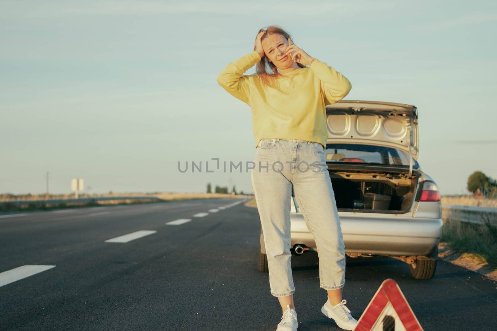 a girl of European appearance in a yellow sweater and jeans stands on the road near a broken car and speaks on the phone upset and holding her head, on the left there is a place for an inscription by PopOff