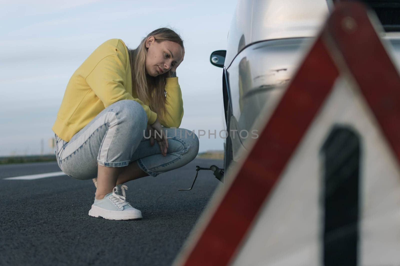 a girl in a yellow sweater sits on the pavement near a broken car, upset, worried, there is a white-red emergency stop sign nearby. there is a place for an inscription girl sits in depression by PopOff