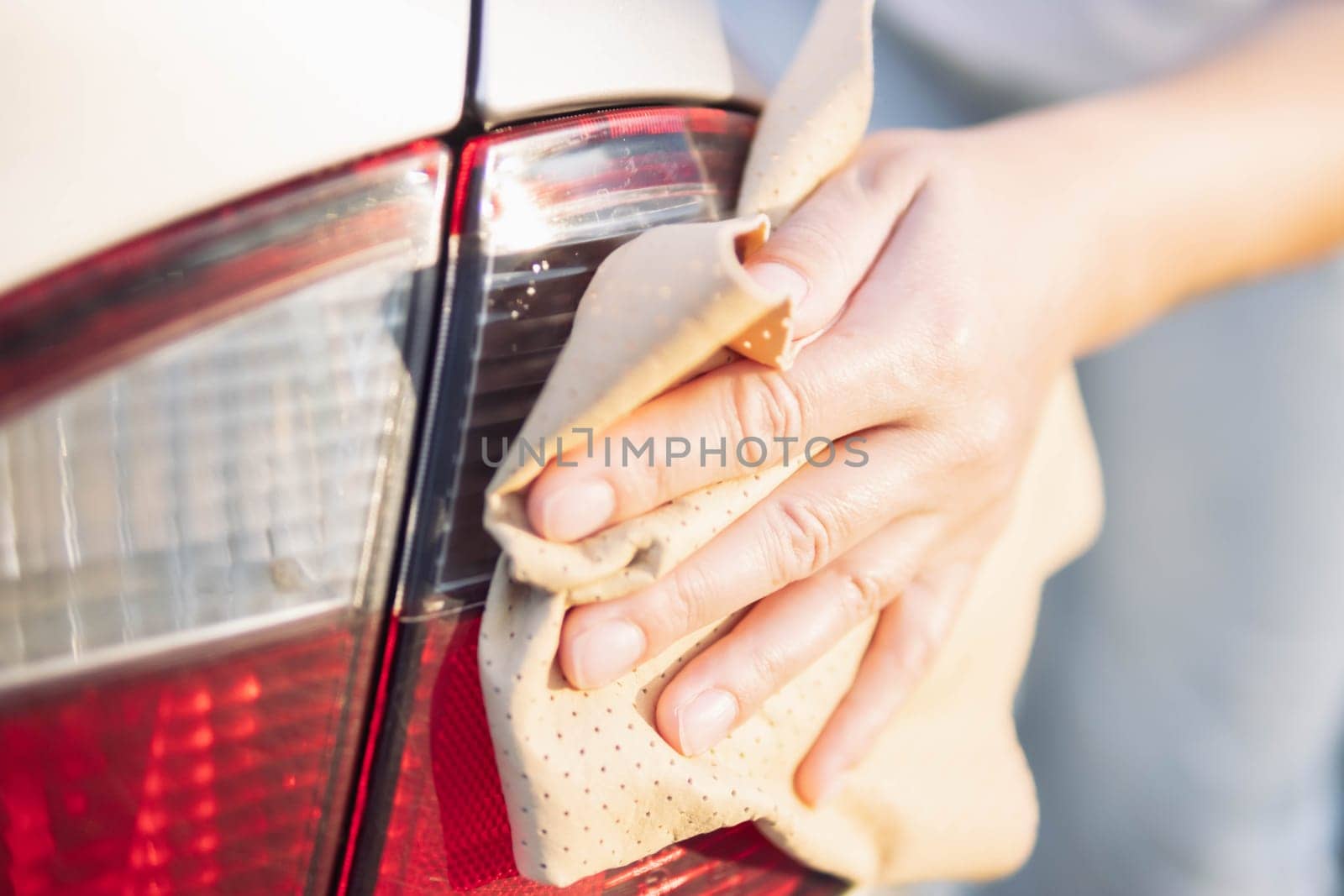 close-up female hand with a brown rag for glasses, wipes the rear lights on the car, after washing. Close-up, there is a place for an inscription. by PopOff