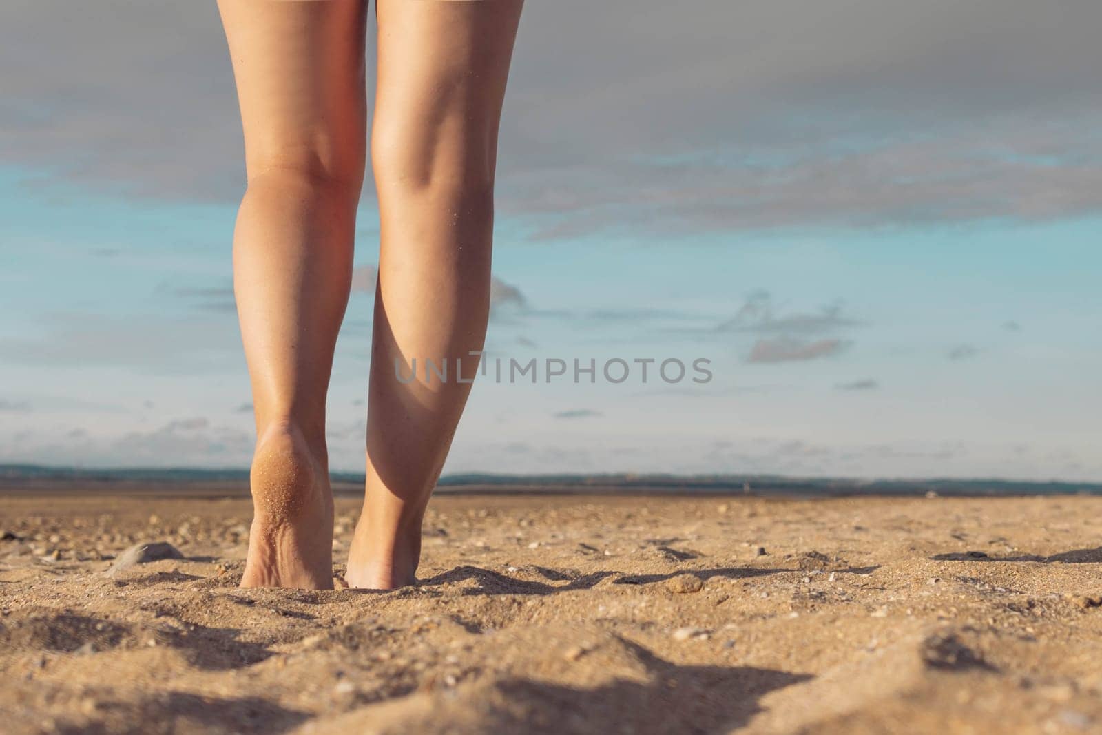 female legs against the background of the sky and sand on the beach. Female legs against the background of a sunset. Beautiful landscape, with a place for an inscription on the right side by PopOff