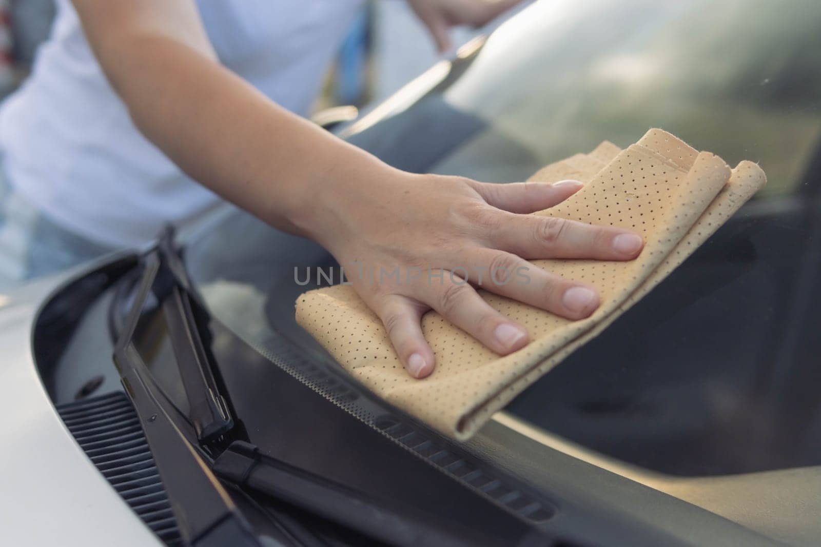 A girl in a white t-shirt wipes the window in the car with a yellow special window cloth.Close-up of a hand and a rag.Work and cleanliness concept. by PopOff