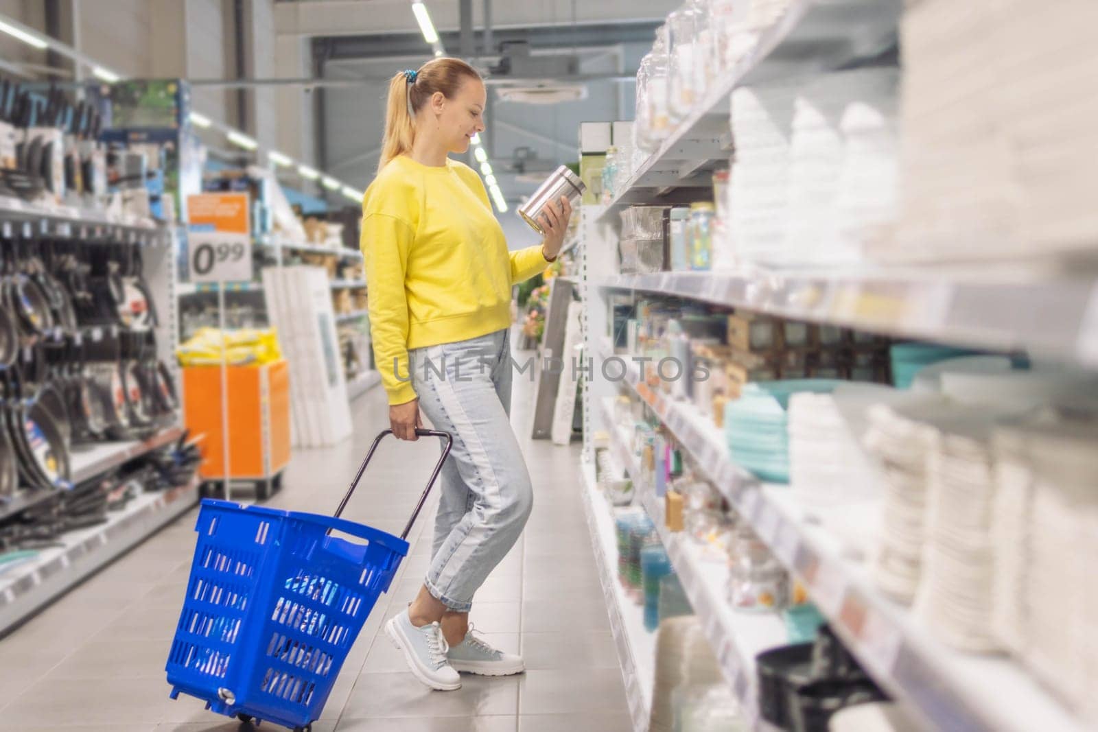 Cheerful girl makes purchases in a dishware store, chooses beautiful dishes for home. High quality photo a girl with blond hair of European appearance in jeans and a yellow sweater stands