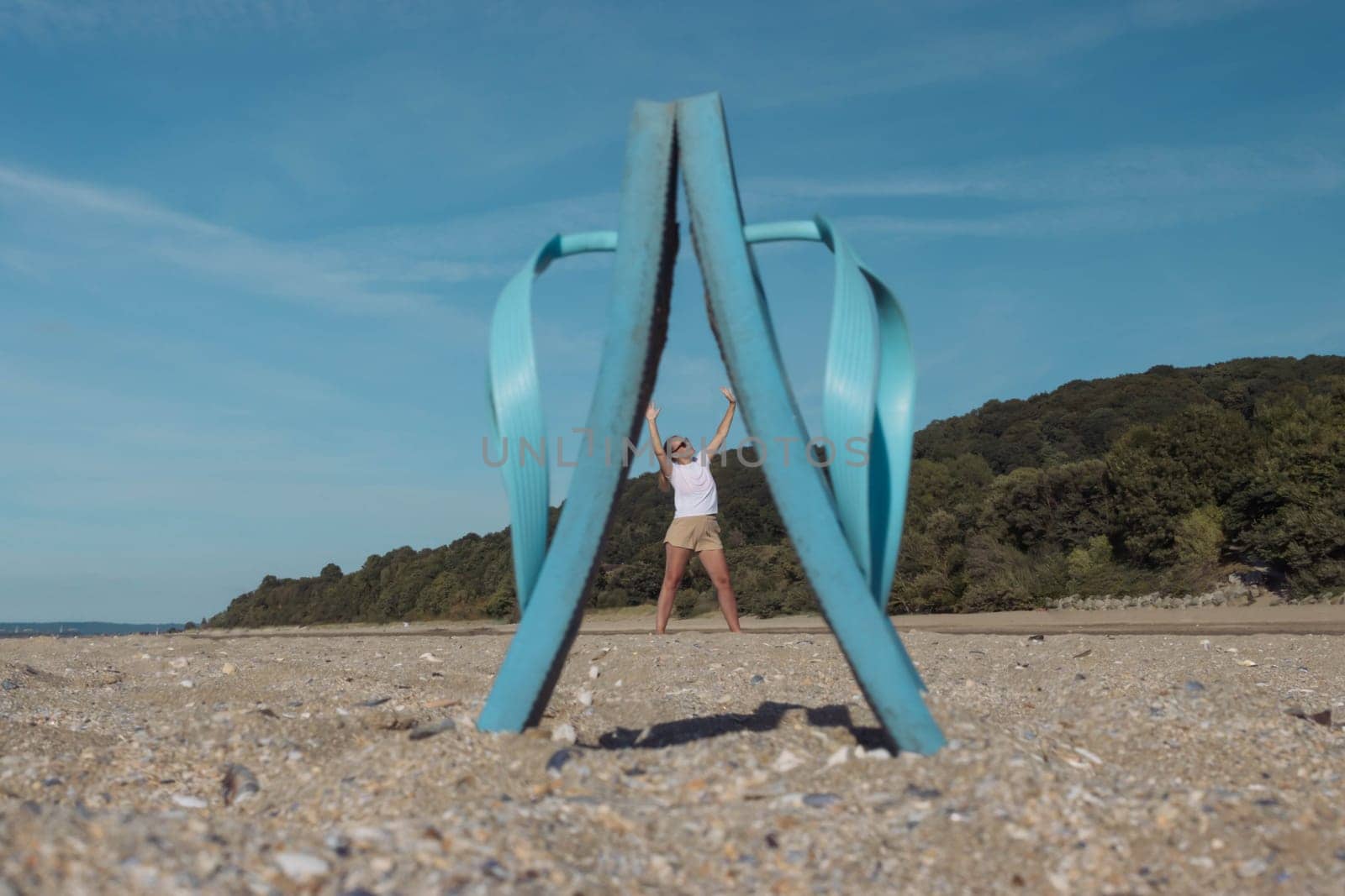 close-up of blue flip-flops standing on the sand between them a small photo of a girl standing between slippers with her hands up.Creative photo and idea for a photo on the beach.High quality photo