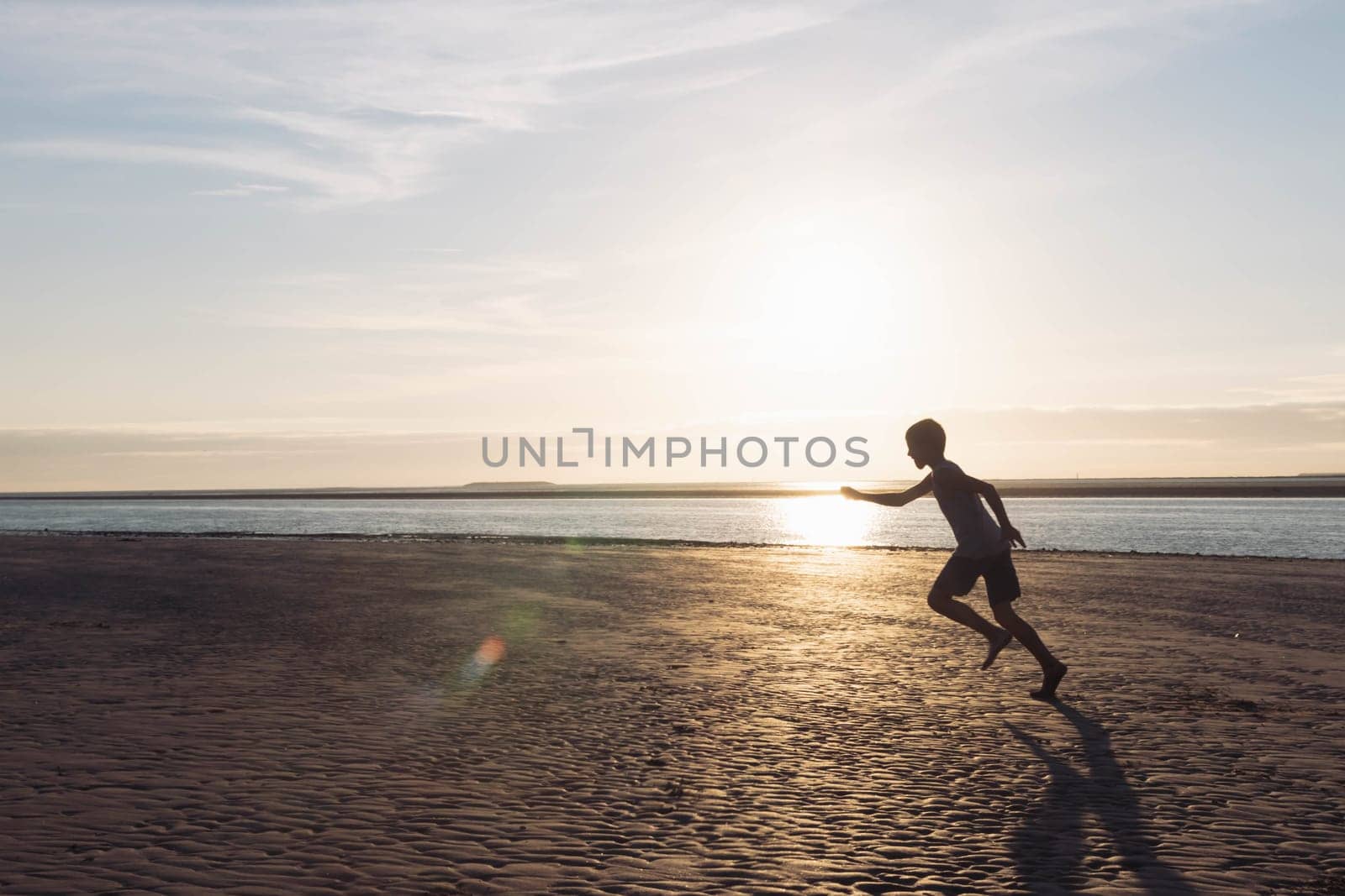 a boy runs on the beach at sunset, a silhouette of a child running on the beach on the sand near the water, there is a place for an inscription. High quality photo