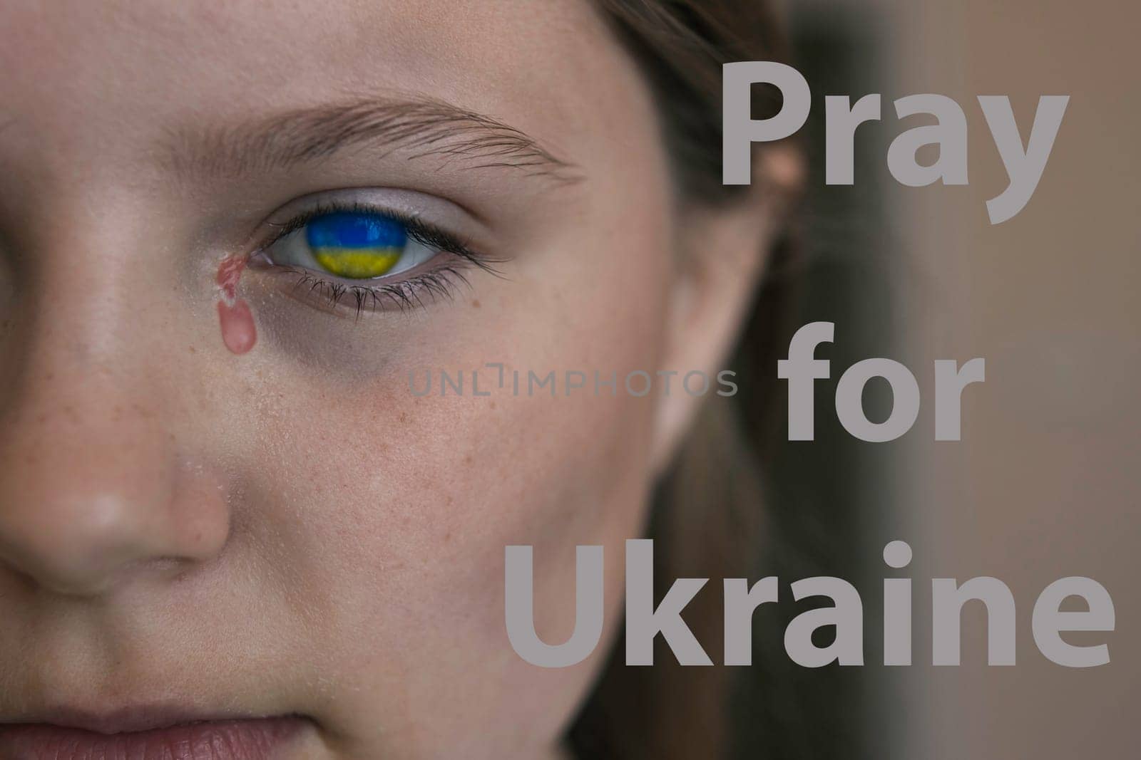 A sad face of a child with the eyes of the flag of Ukraine and a tear with blood. Close-up. Then pray for Ukraine on the right side.War in Ukraine. High quality photo