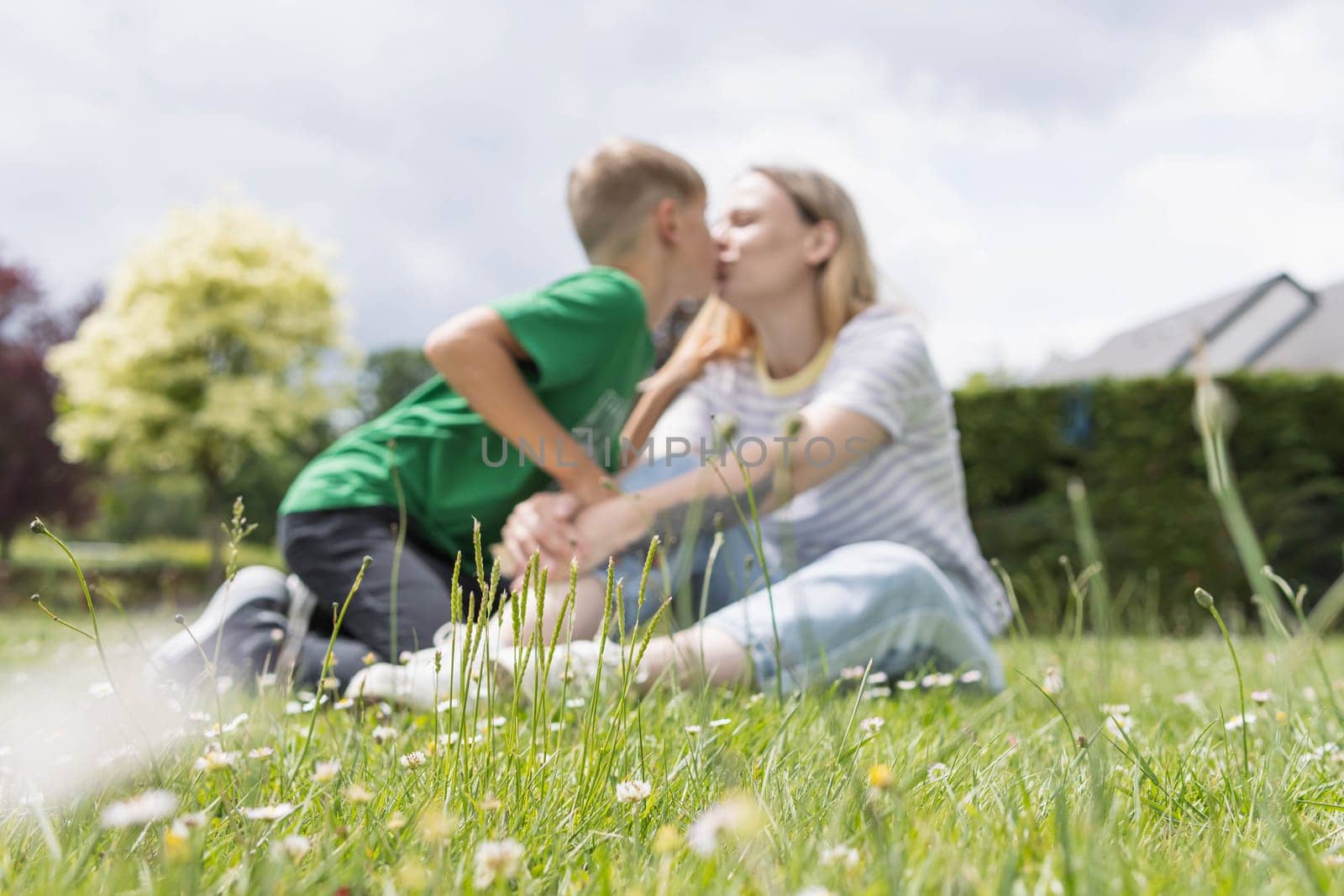 mom and son are sitting on the green grass in the park and kissing by PopOff