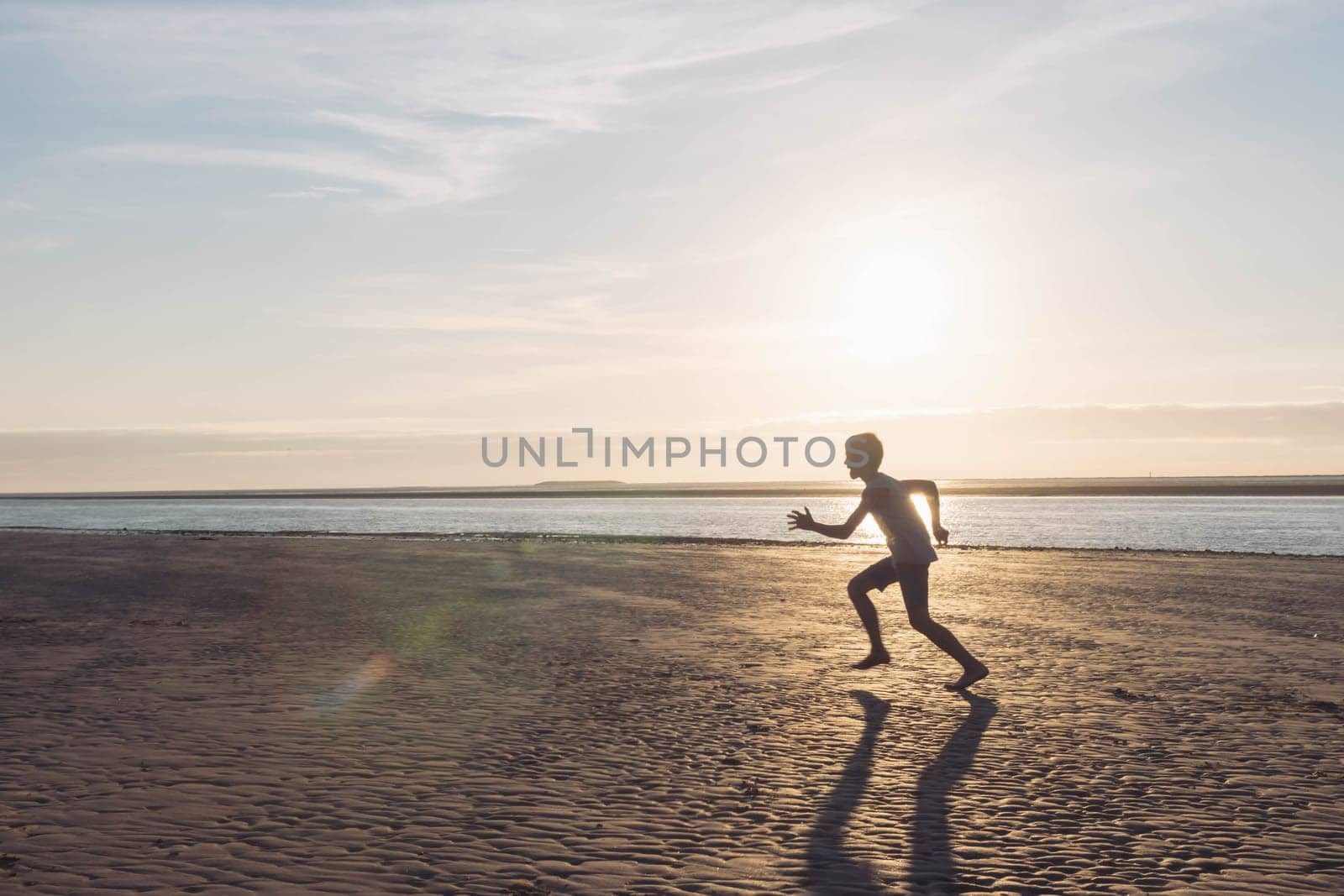 a silhouette of a child running on the beach on the sand near the water, at sunset there is a place for an inscription by PopOff