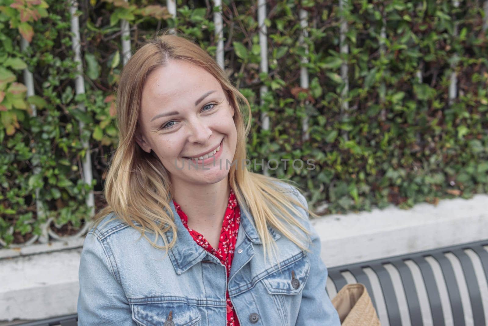 a girl with blond hair in a denim jacket sits in a park dreaming and smiling close-up, portrait .human emotions by PopOff