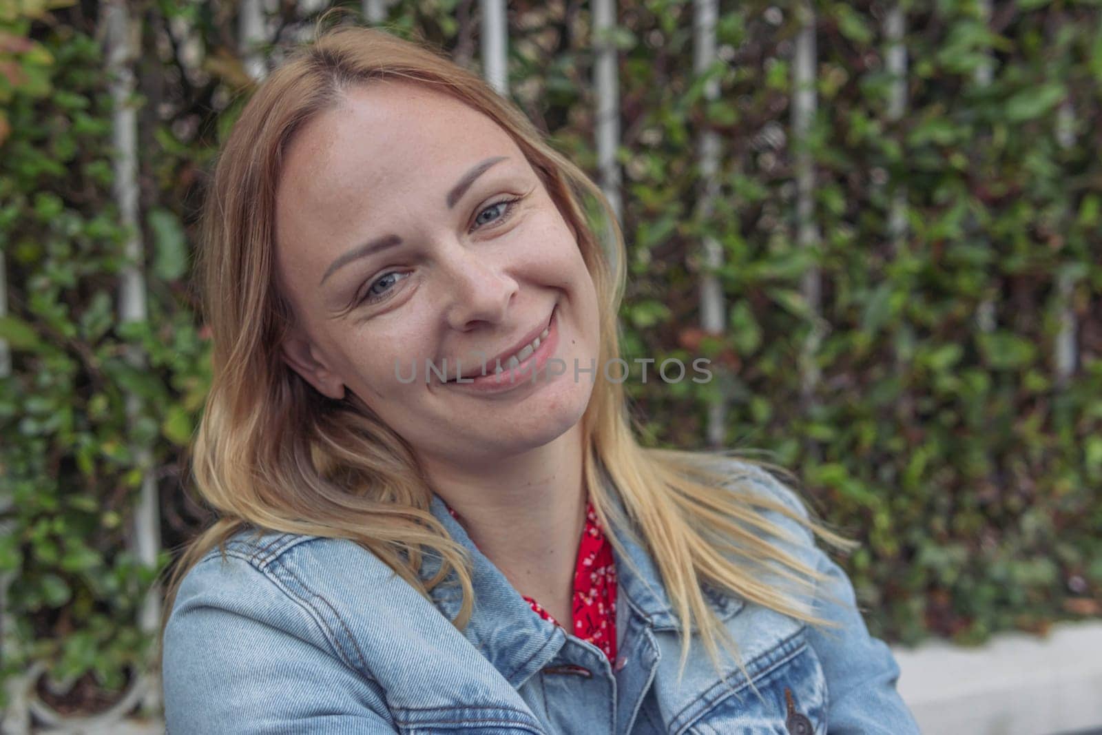 a girl of European appearance with blond hair in a denim jacket sits in a park and thinks daydreams holding her hand to her head close-up portrait a girl . High quality photo