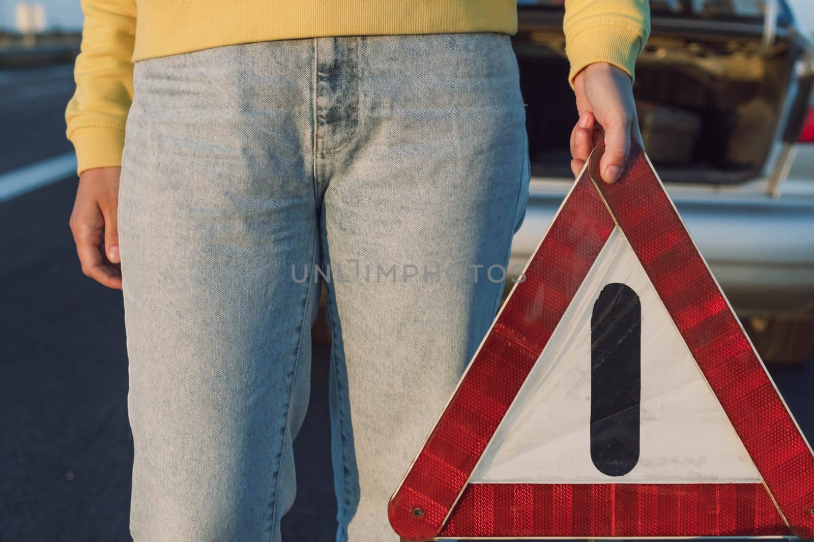 a girl puts an emergency stop sign on the highway near a broken car close-up on the sign. A car breakdown on the highway, there is a place for an inscription. High quality photo