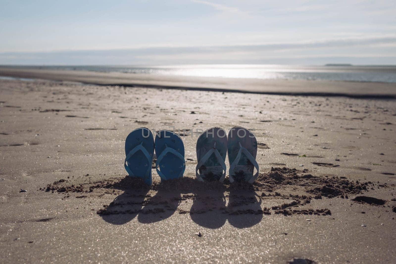 on the beach in the sand buried two pairs of beach slippers at sunset photo taken, beautiful and creative beach background with a place for an inscription by PopOff